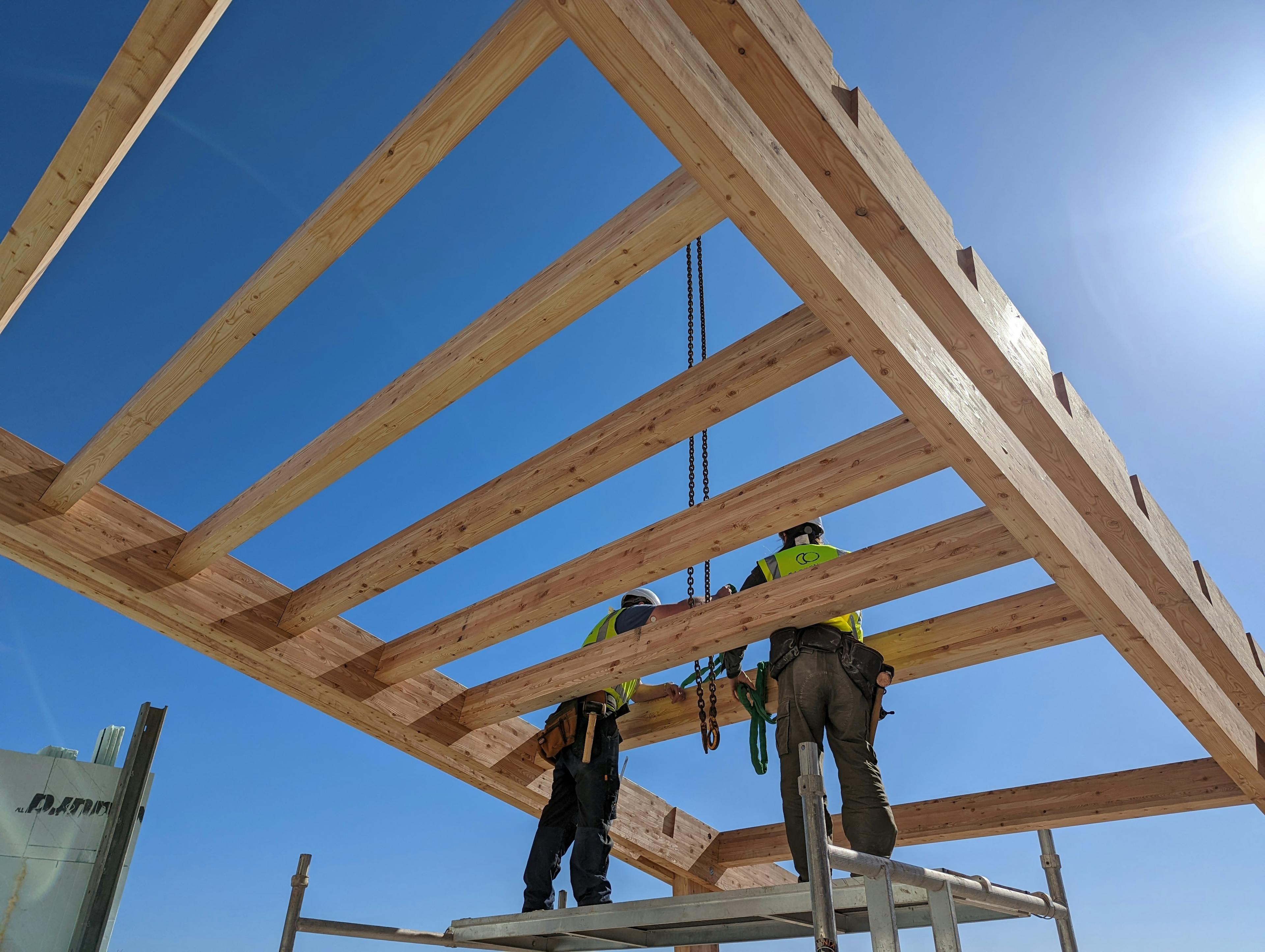 Carpenters install a larch glulam frame with a blue sky behind them