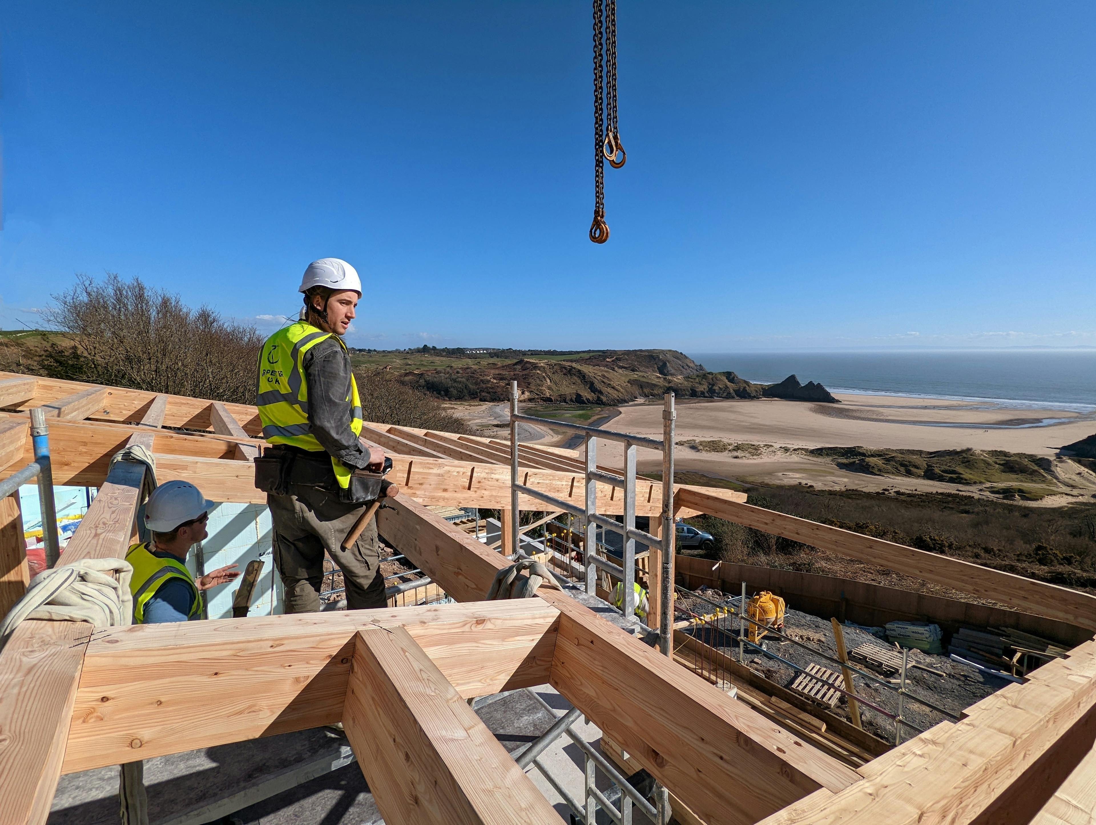 Carpenters install a larch glulam frame on a site overlooking a beach