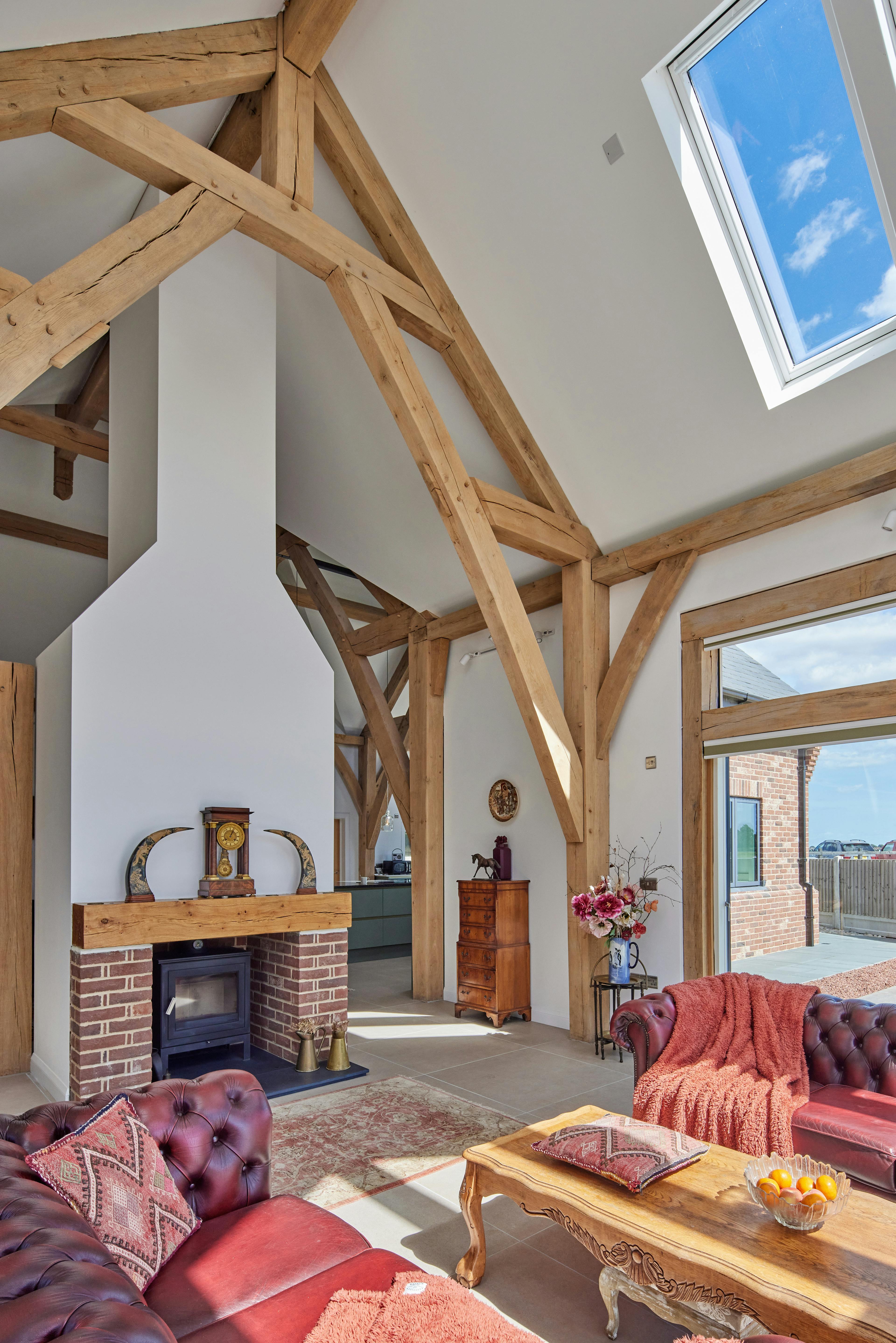 An open plan living sitting area with log burner in an oak framed home with a double height vaulted ceiling.