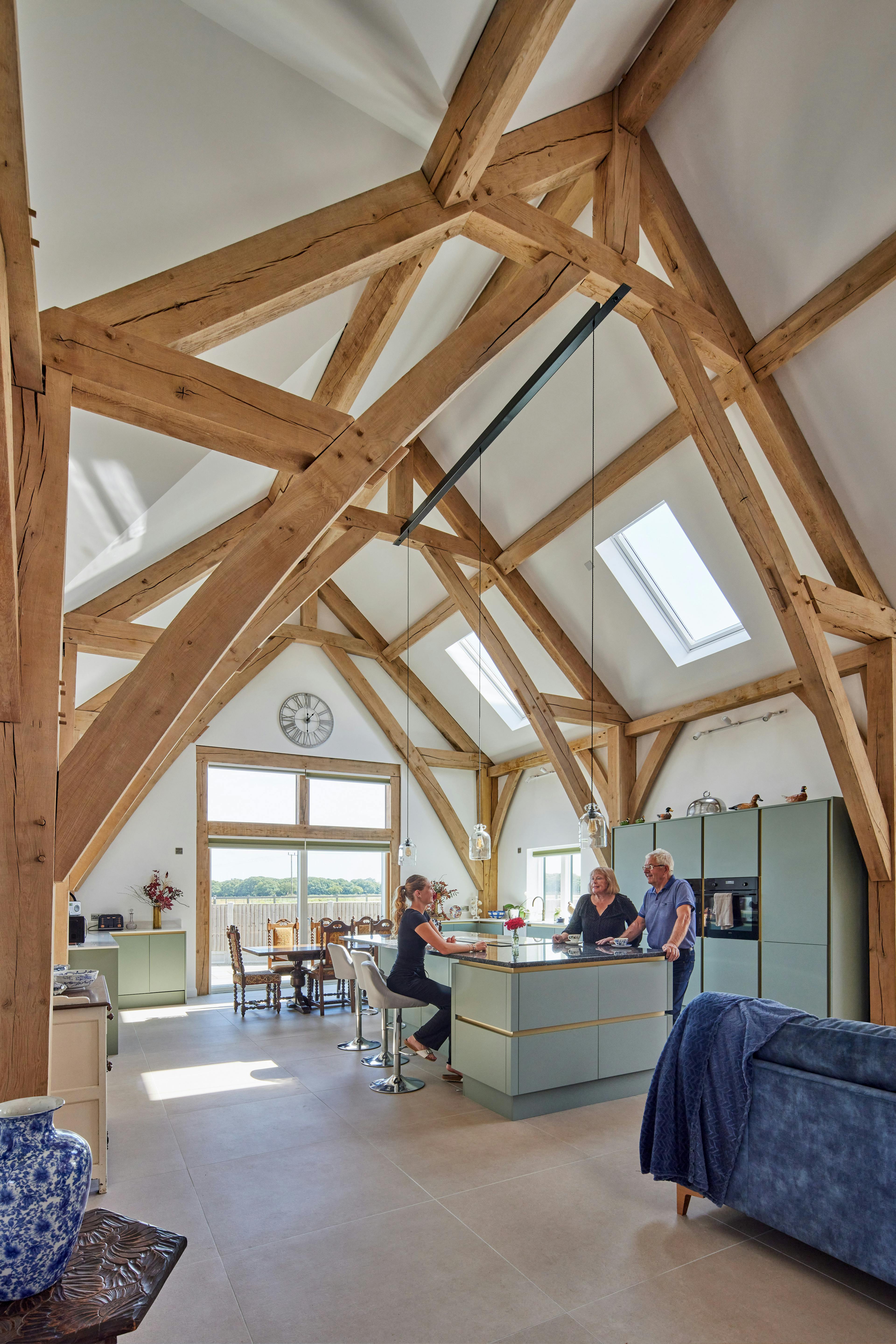 People sitting at a kitchen island in an open plan dining and kitchen area in an oak framed home with a double height vaulted ceiling.