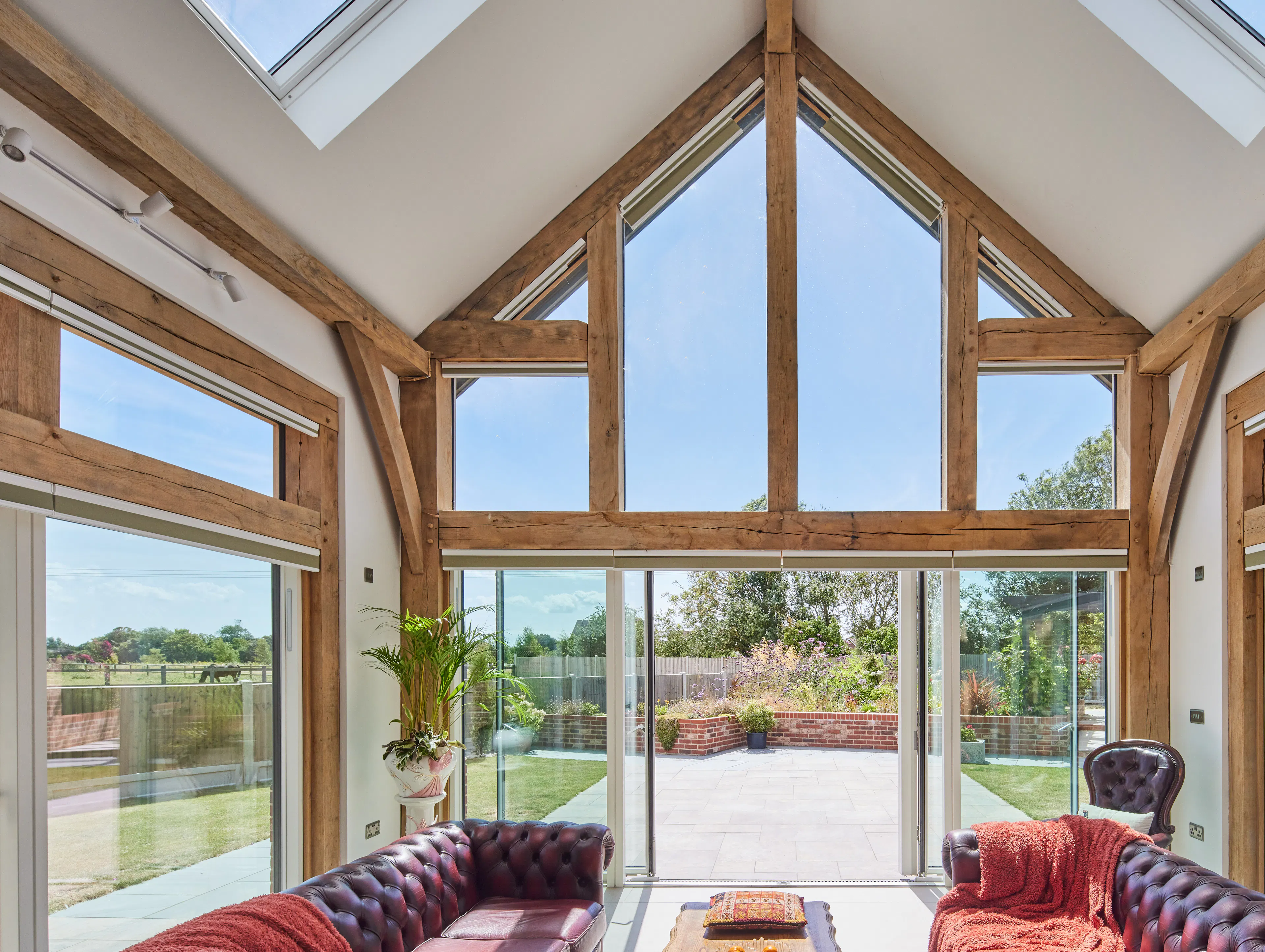 A double height oak framed open plan sitting room with red leather sofas in and a glazed gable end.