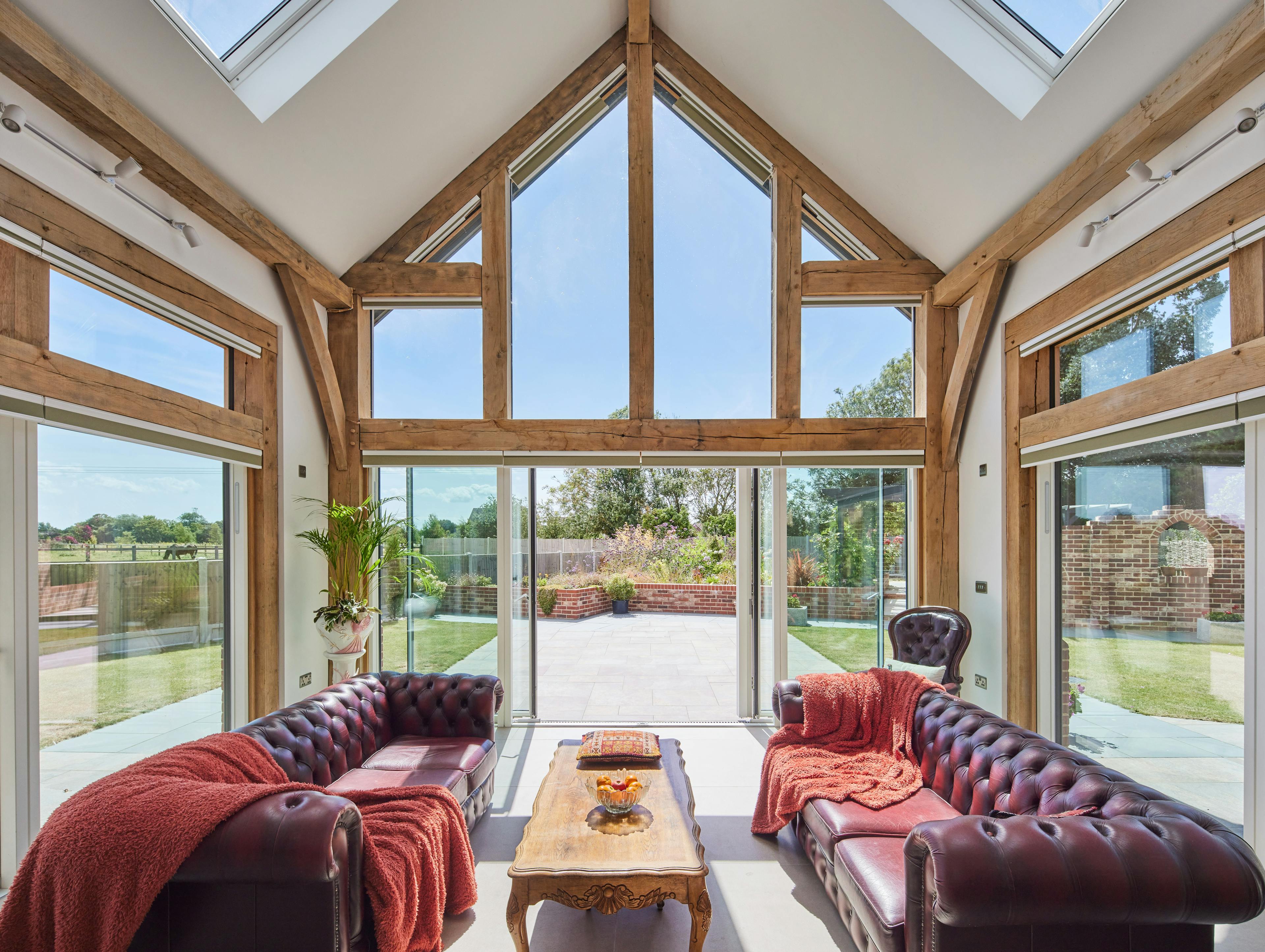 A double height oak framed open plan sitting room with red leather sofas in and a glazed gable end.