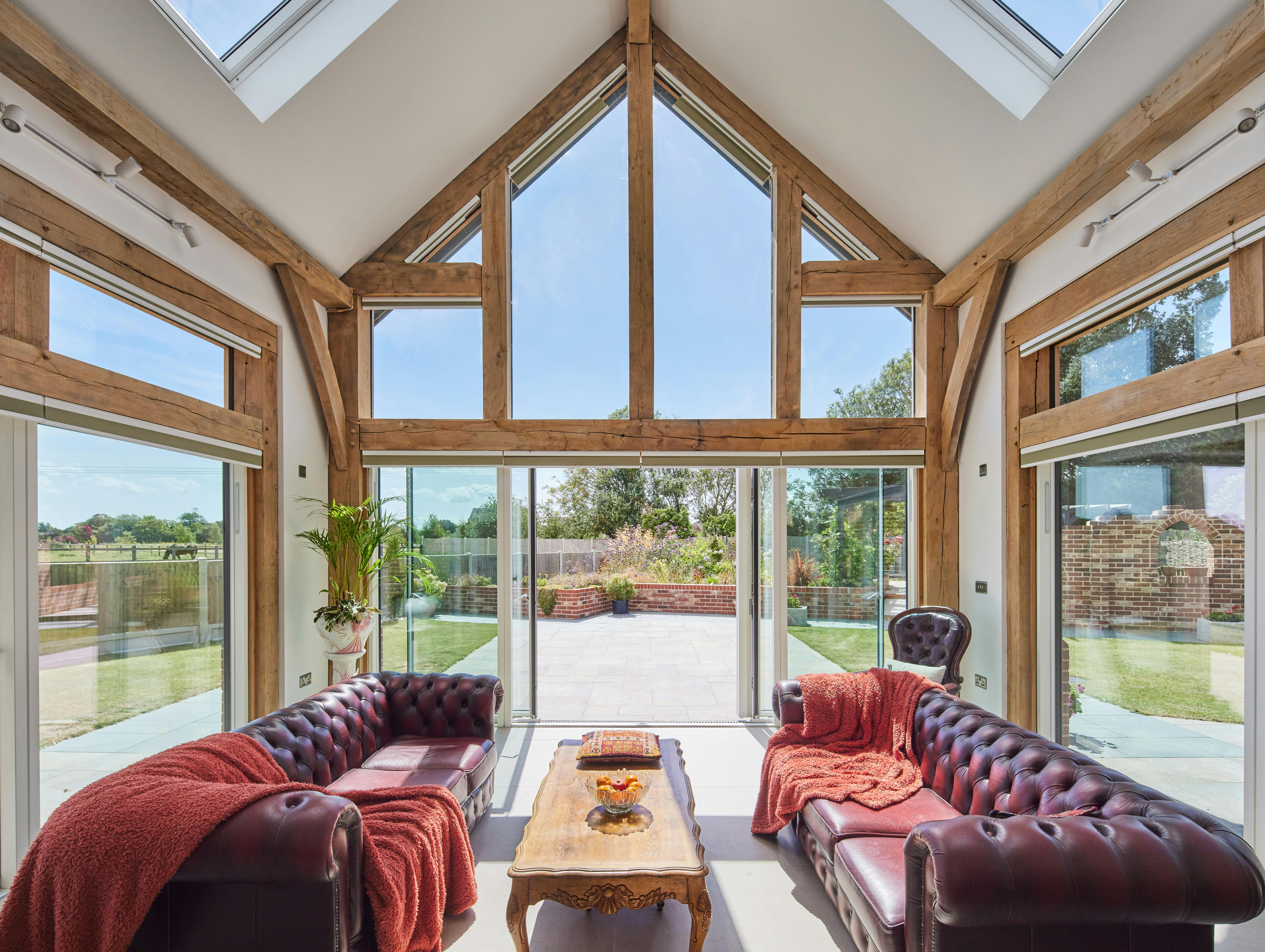 A double height oak framed open plan sitting room with red leather sofas in and a glazed gable end.
