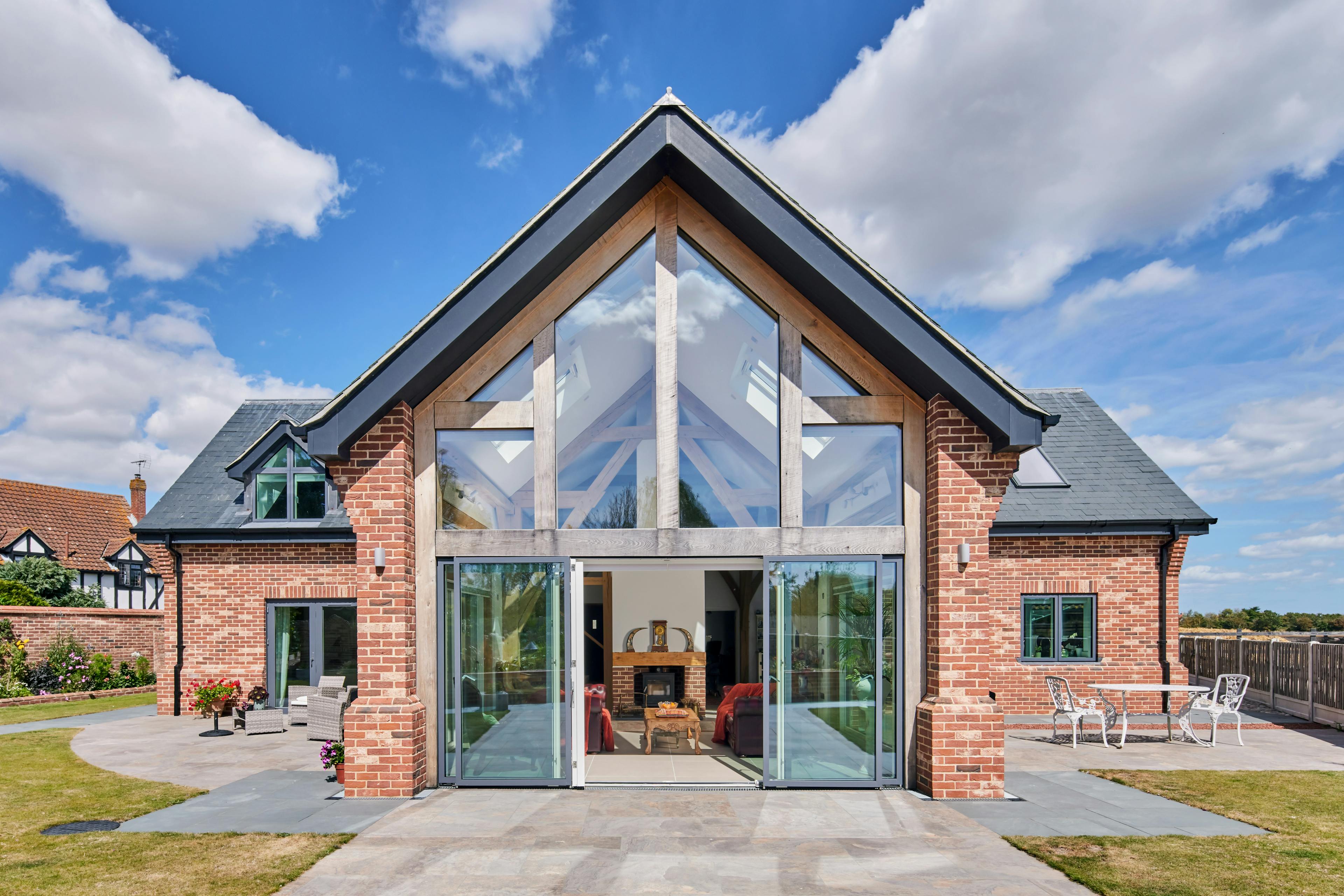 An exterior view of an oak framed house in a landscaped garden which has been finished with red brickwork and grey roof tiles.