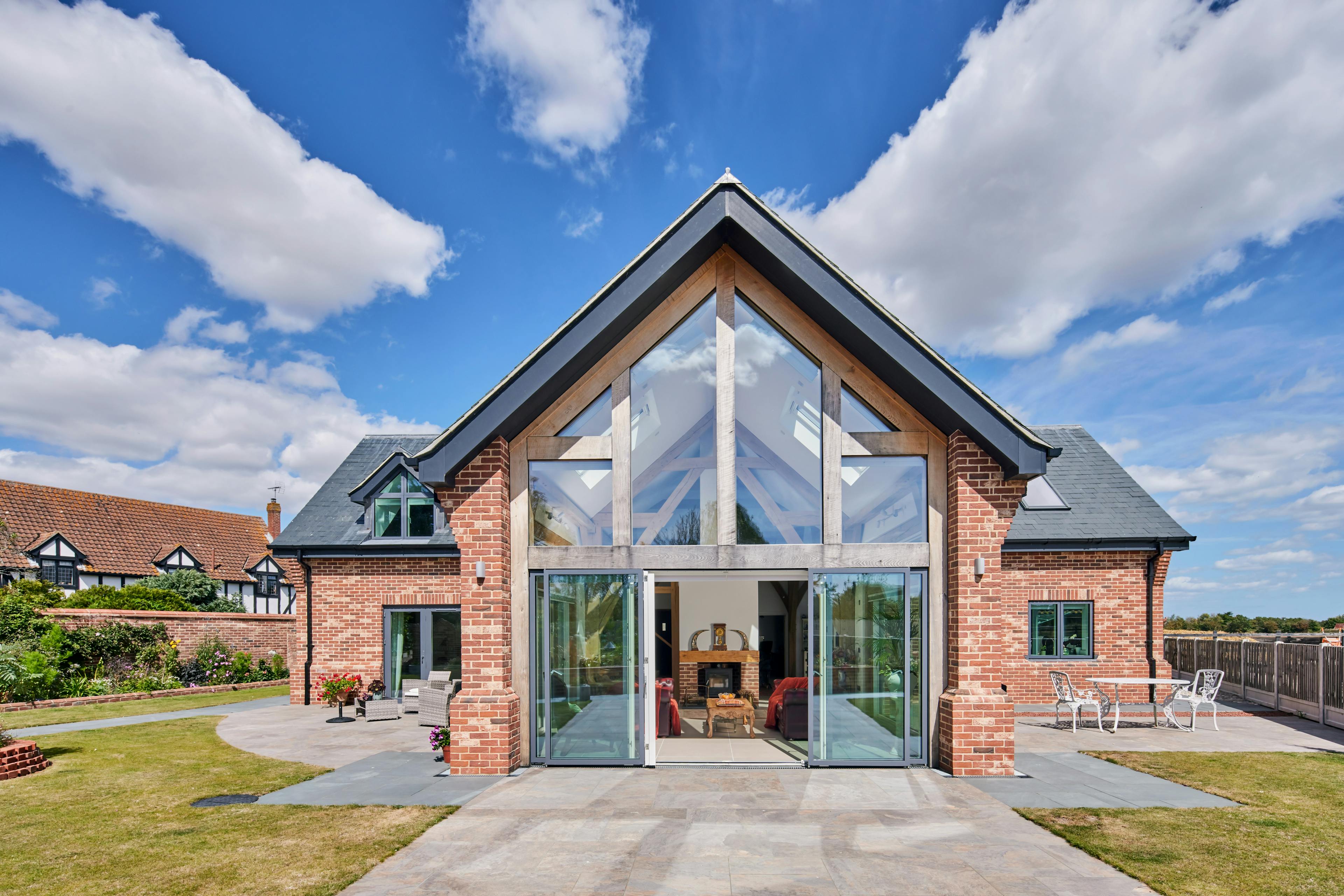 An exterior view of an oak framed house in a landscaped garden which has been finished with red brickwork and grey roof tiles.