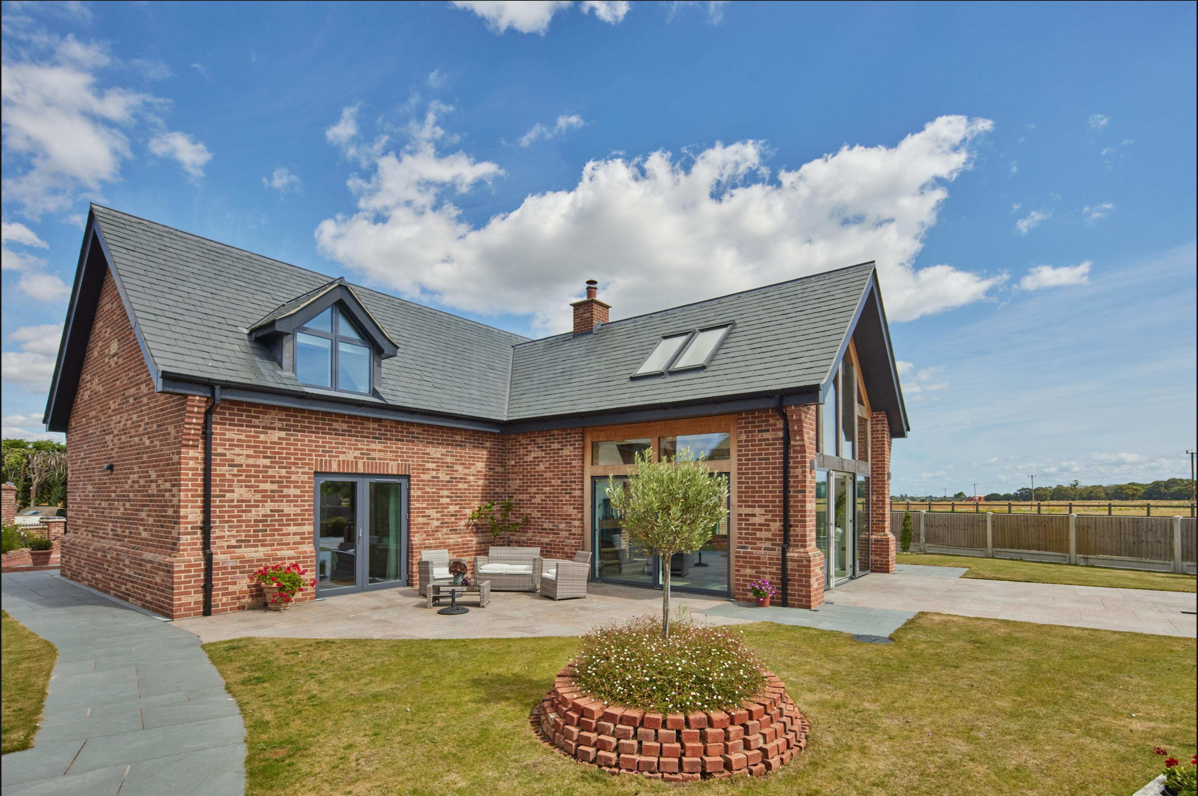 An exterior view of an oak framed house in a landscaped garden which has been finished with red brickwork and grey roof tiles.
