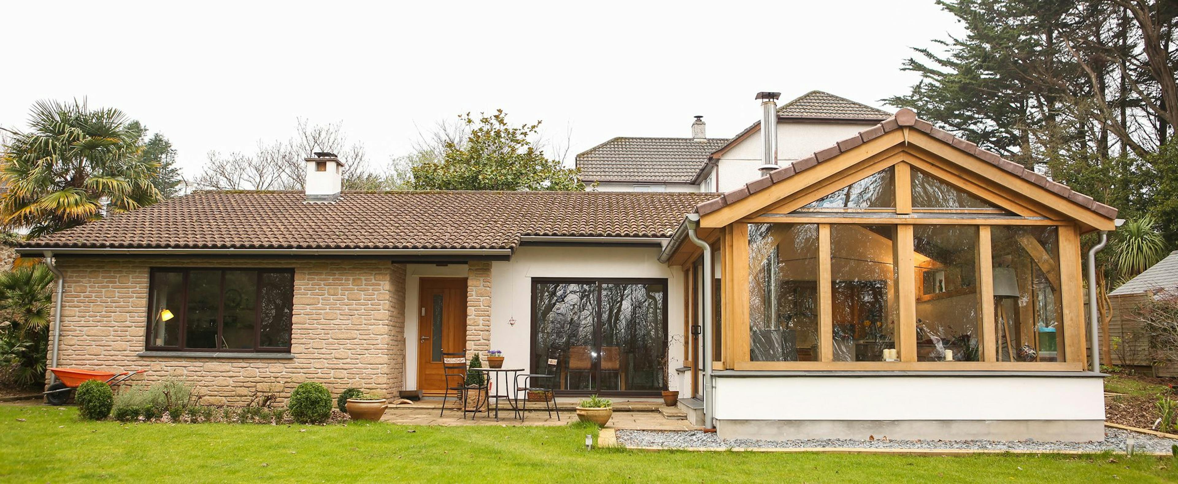 Oak-framed extension with a gable roof, showcasing a spacious living room with large glass doors, seamlessly blending indoor and outdoor spaces in a Cornwall setting