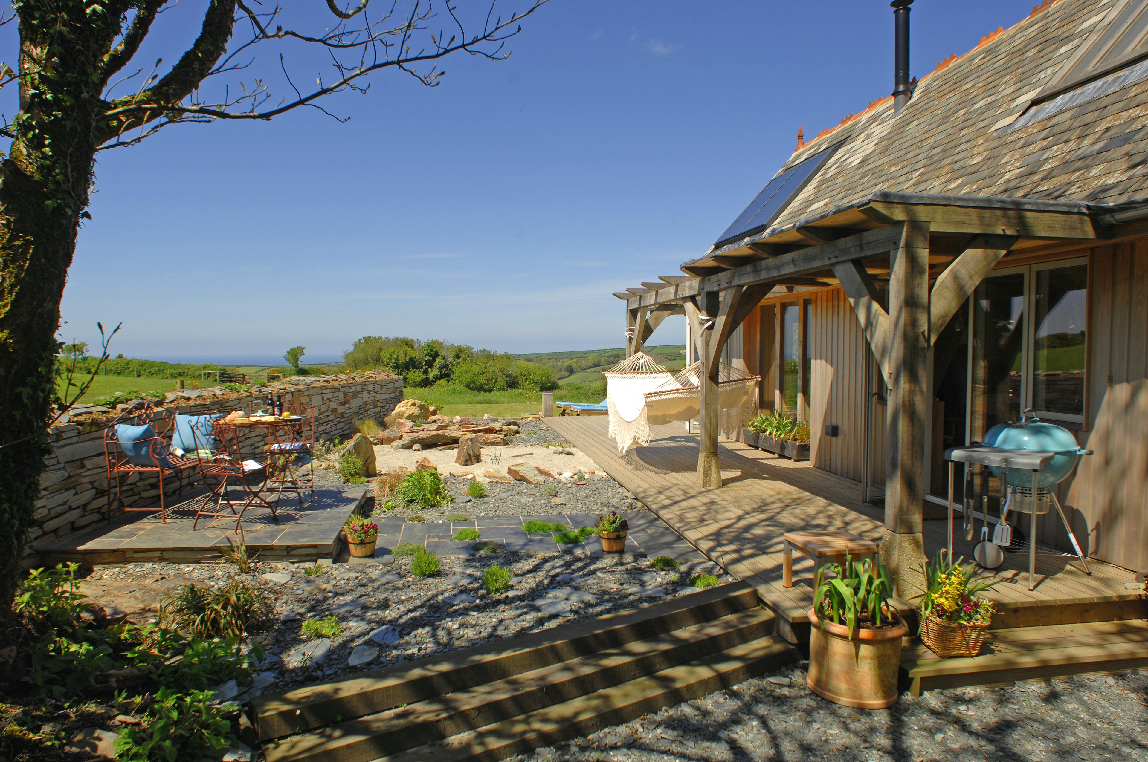 Completed oak-framed house in Cornwall, featuring a charming garden with a pergola, seamlessly blending natural materials with outdoor living space