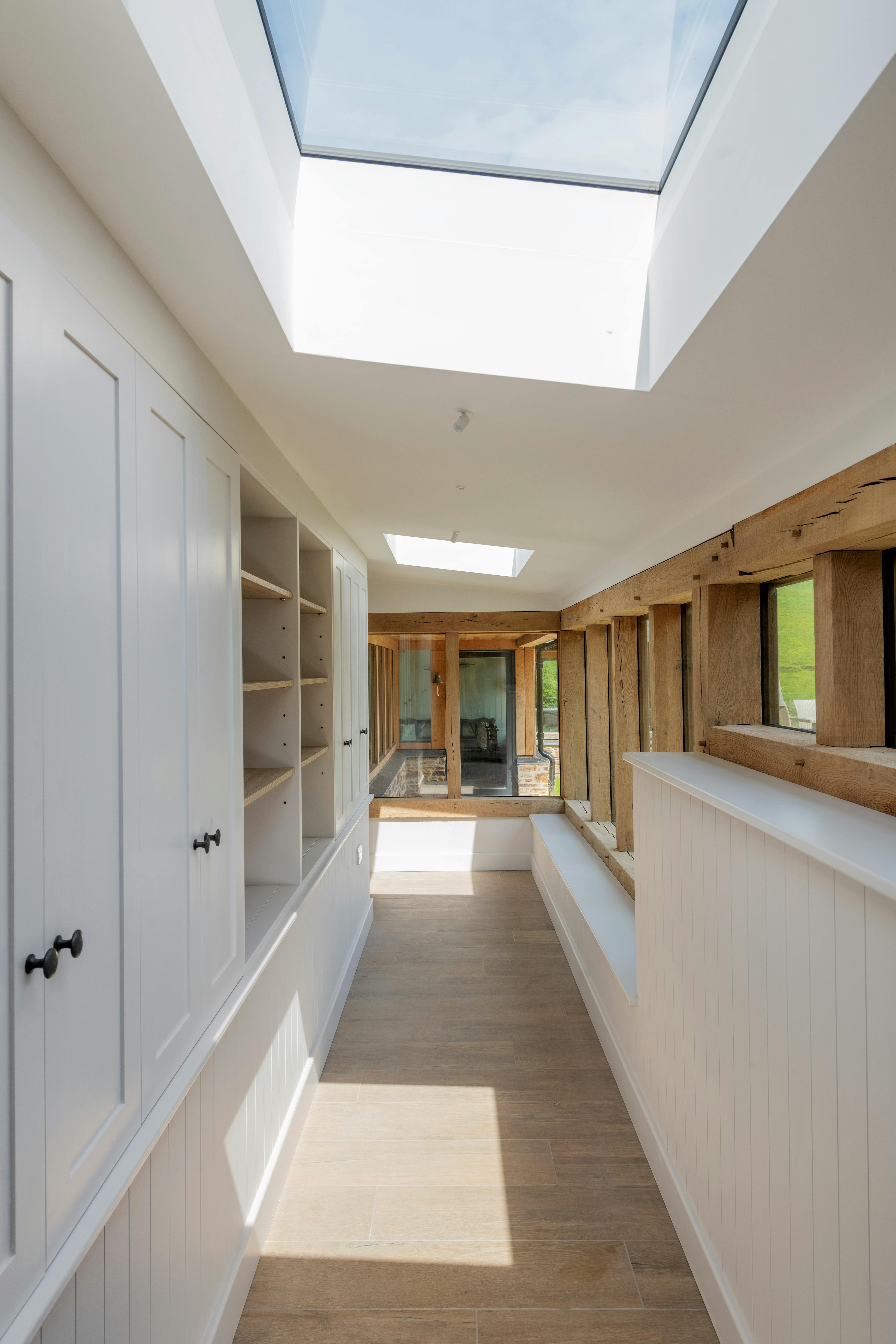 An oak framed corridor with sunshine coming through the rooflights and bespoke cupbaord storage