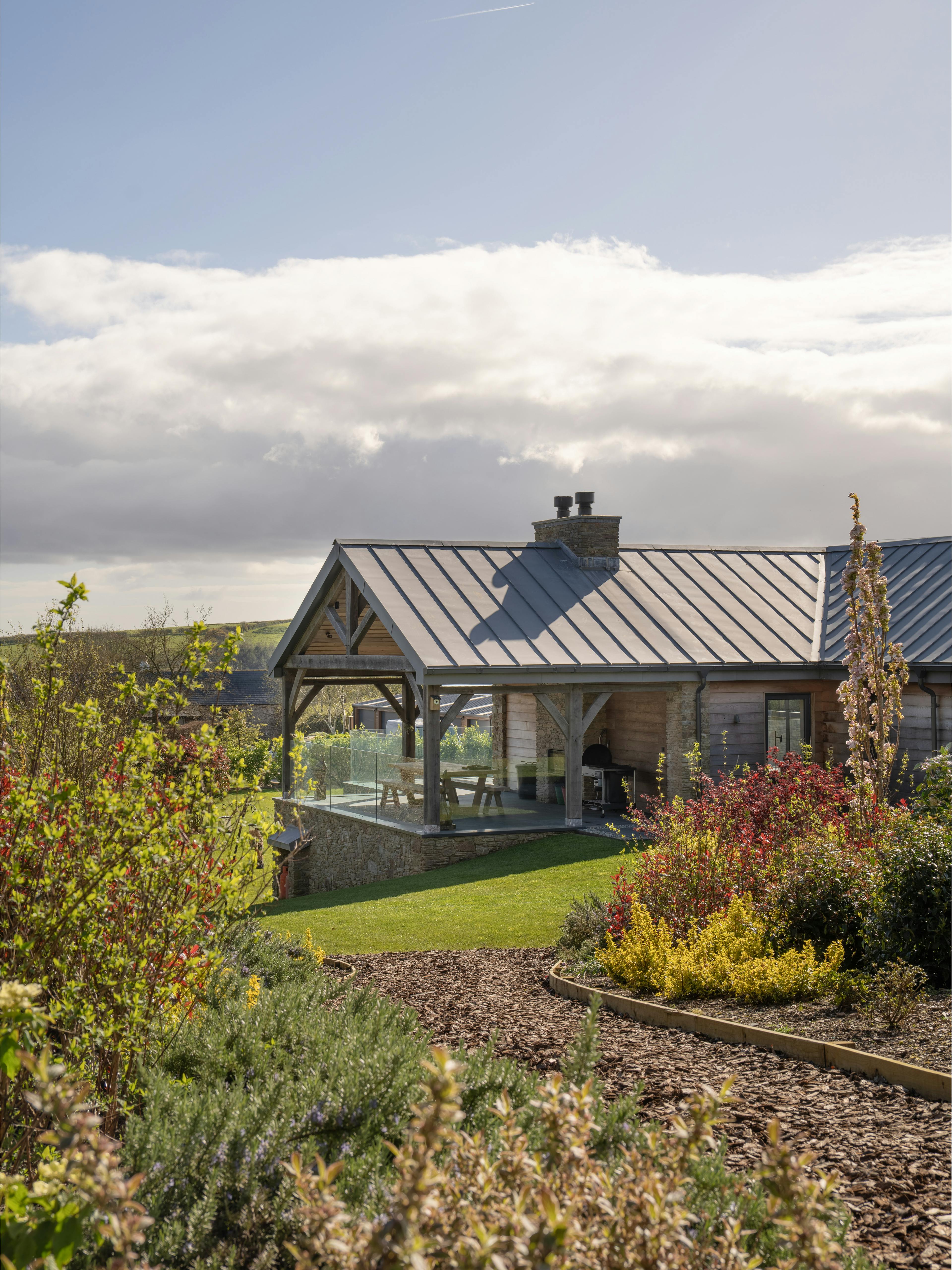 The rear of a stone clad oak framed home with a zinc roof and covered oak framed outdoor eating area