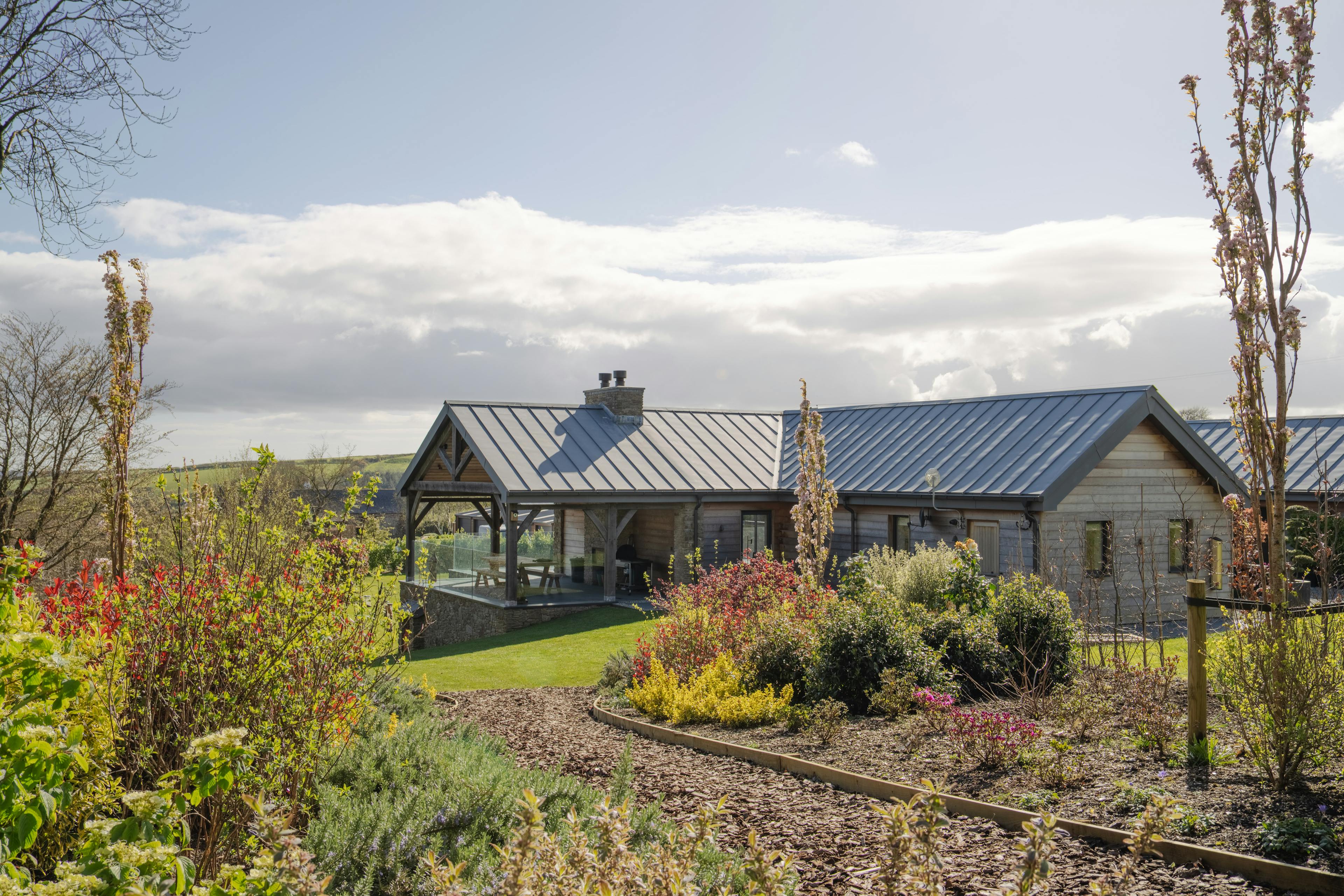 The rear of a stone clad oak framed home with a zinc roof and covered oak framed outdoor eating area