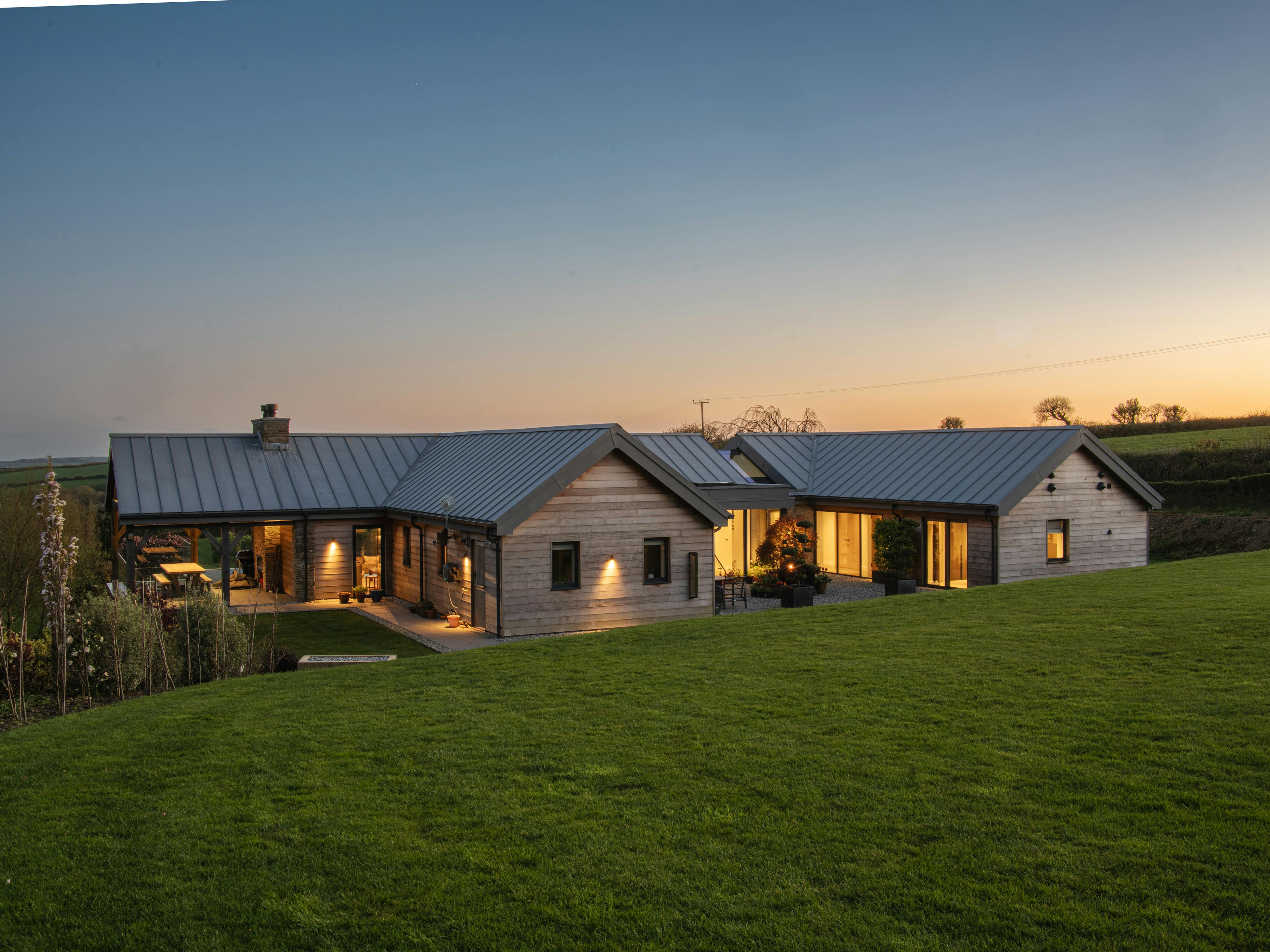 The rear of a stone clad oak framed home with a zinc roof at dusk