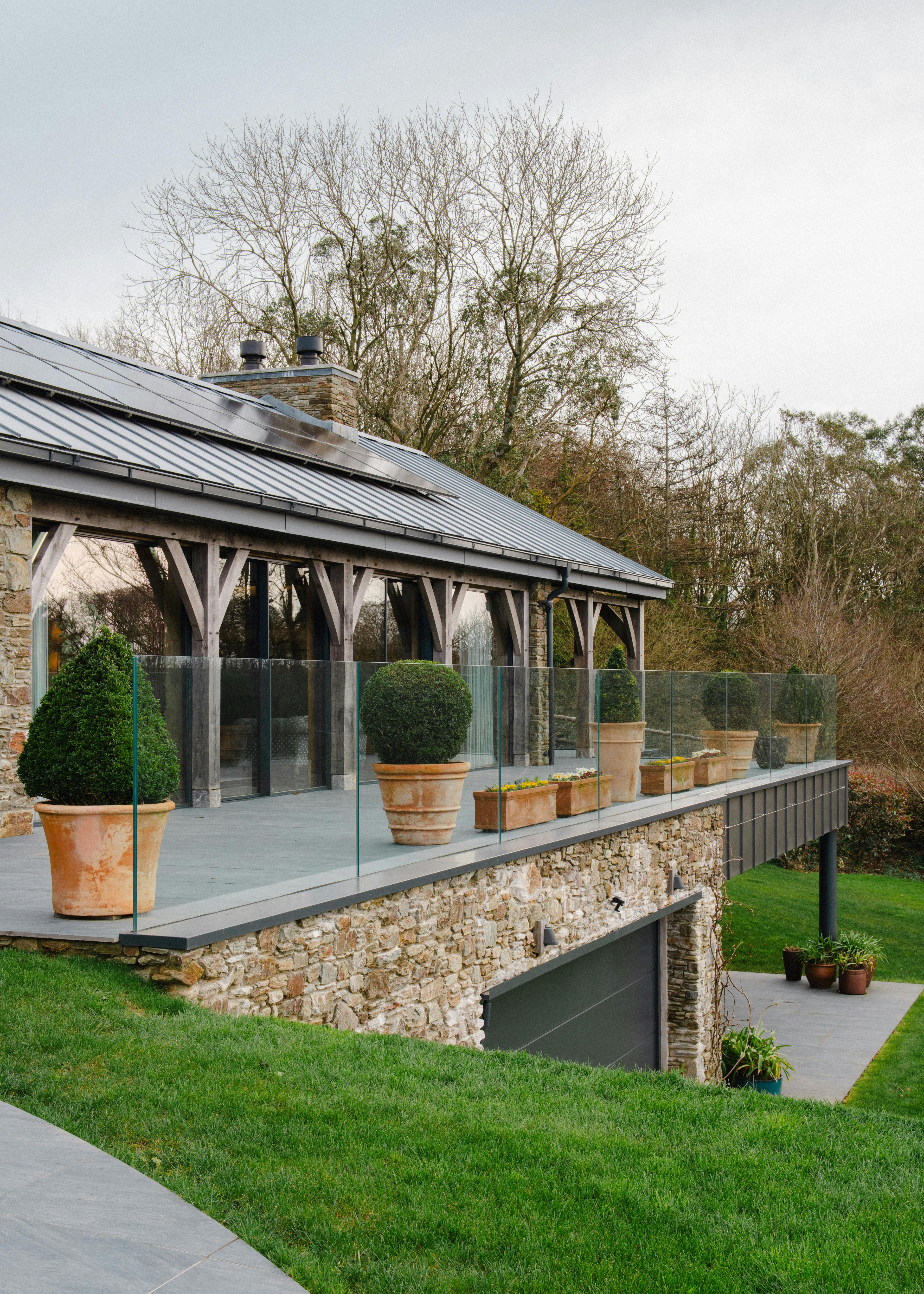 The front of a stone clad oak framed home with a zinc roof, green lawn, exterior oak posts, and driveway 