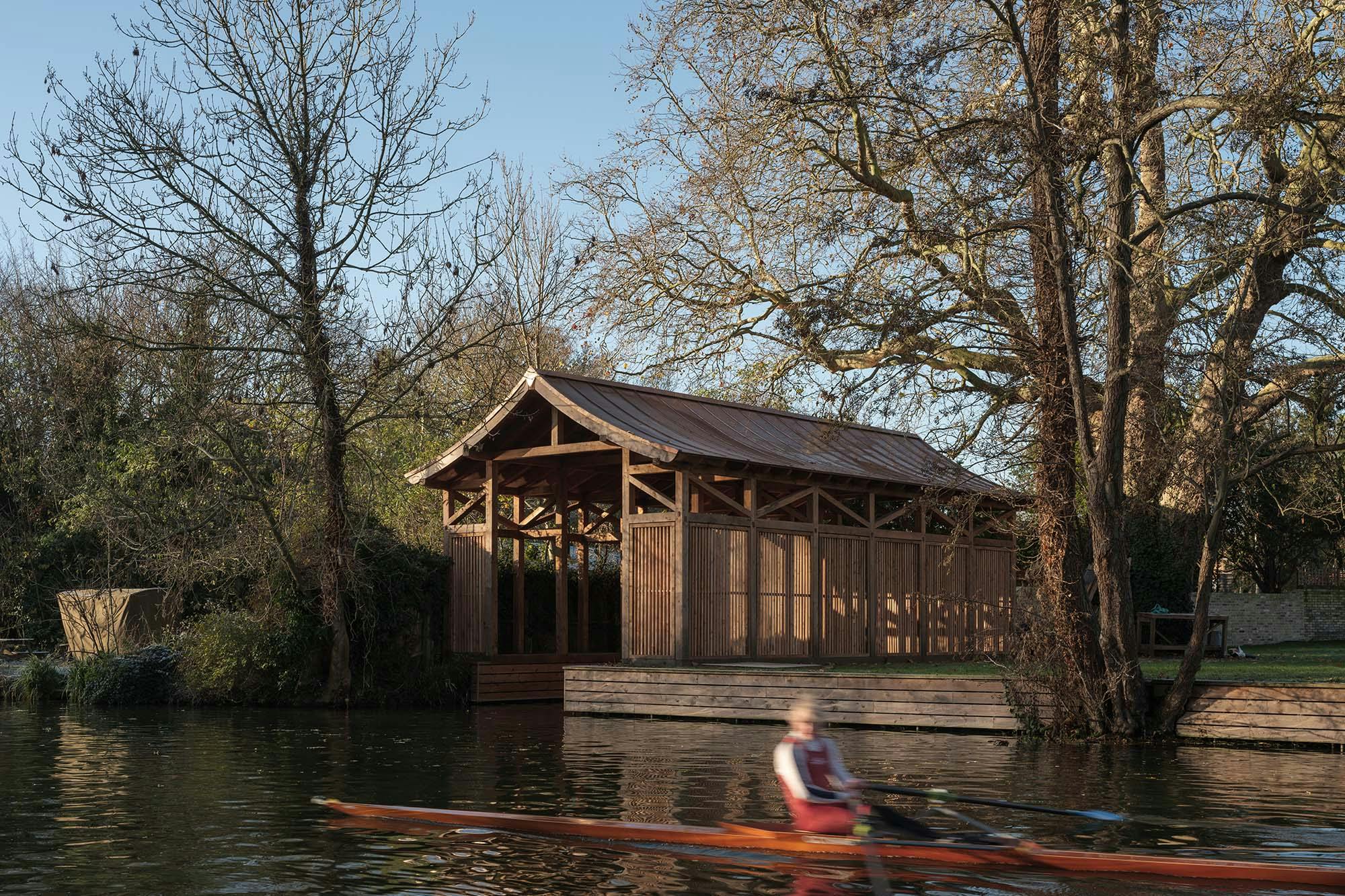 A canoeist on a river in front of a Japanese inspired boathouse