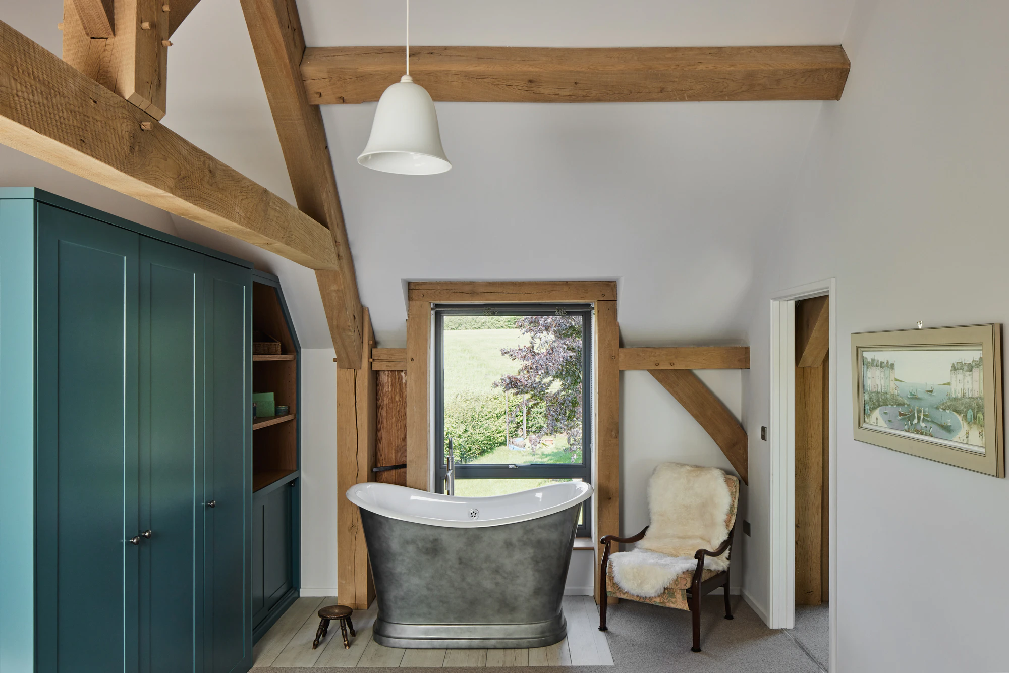 A free standing silver bath and bespoke cabinetry in an oak framed bedroom