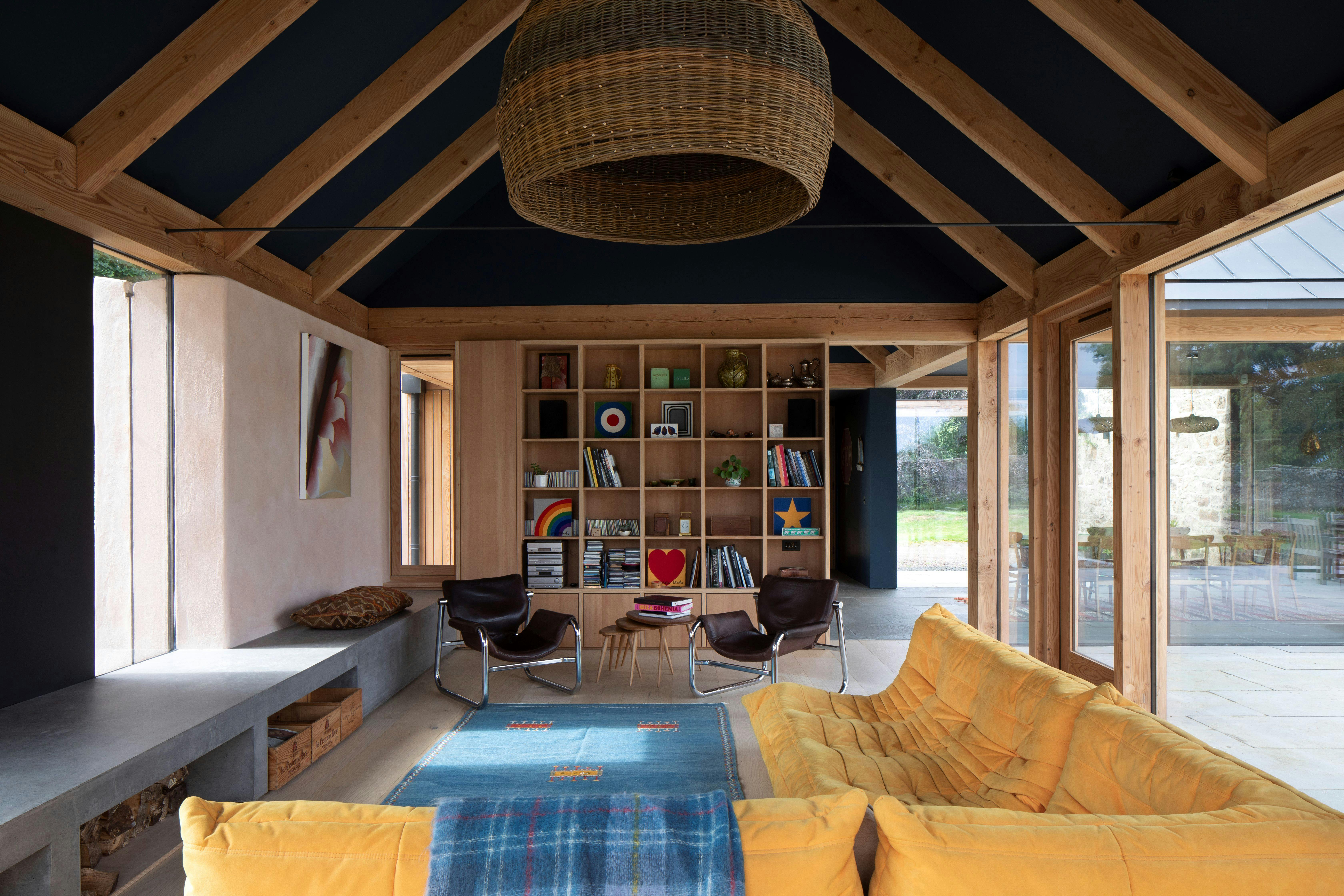 Douglas fir framed sitting room extension with yellow sofa, armchairs, bookcase and glazing
