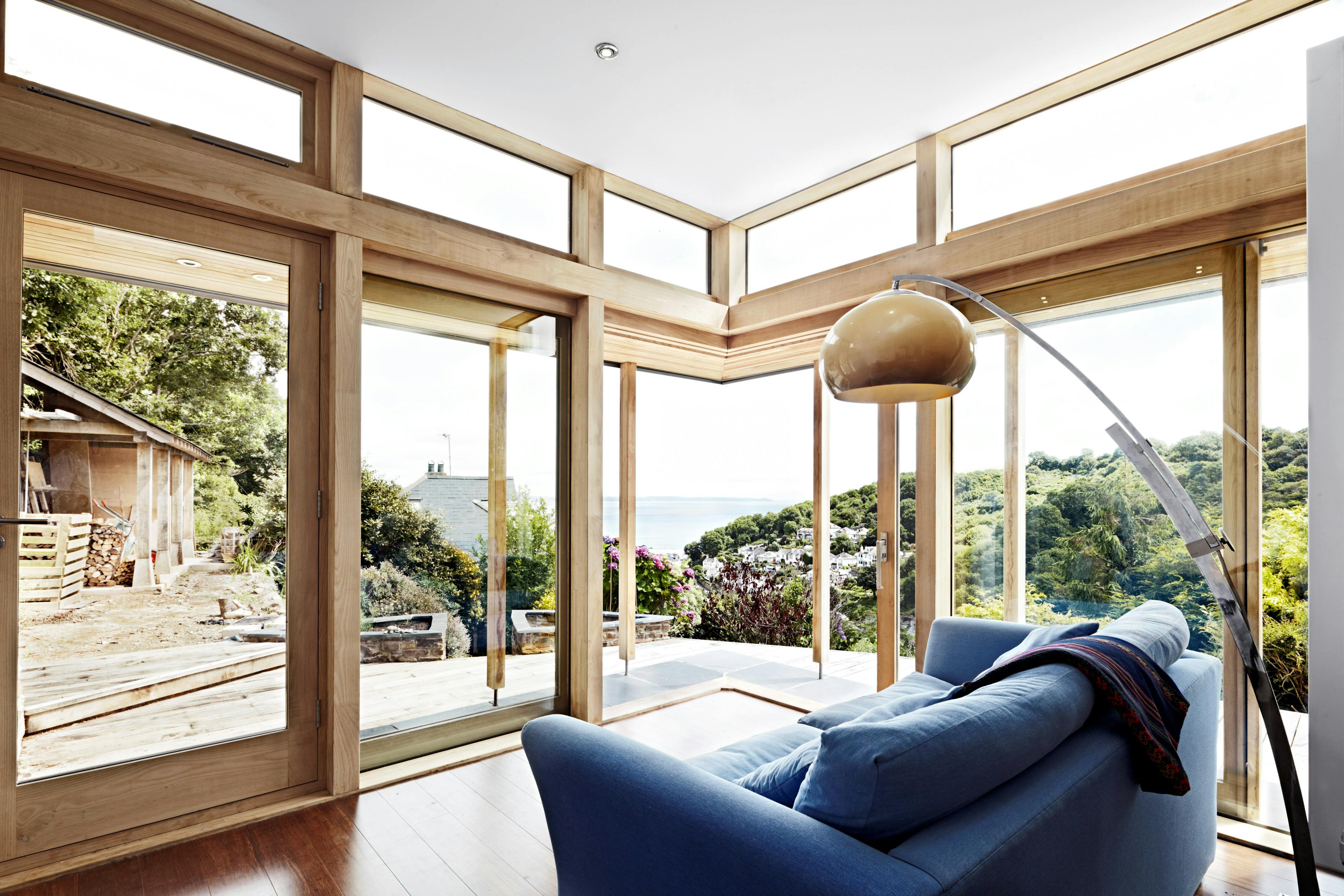 The sitting room of a chestnut glulam extension with wooden decking and views down to the sea
