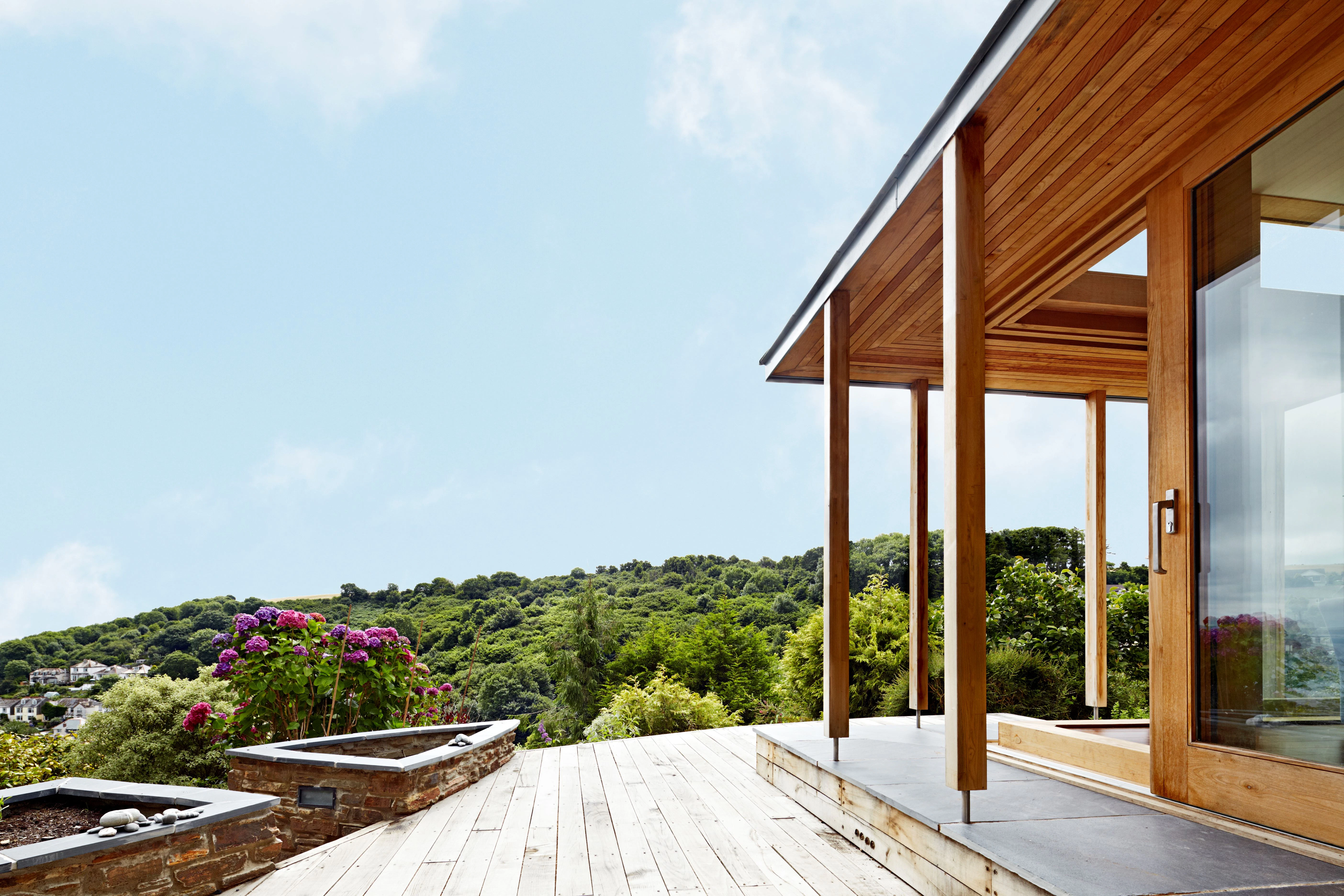 A chestnut glulam extension with wooden decking and views of the surrounding green countryside down to the sea