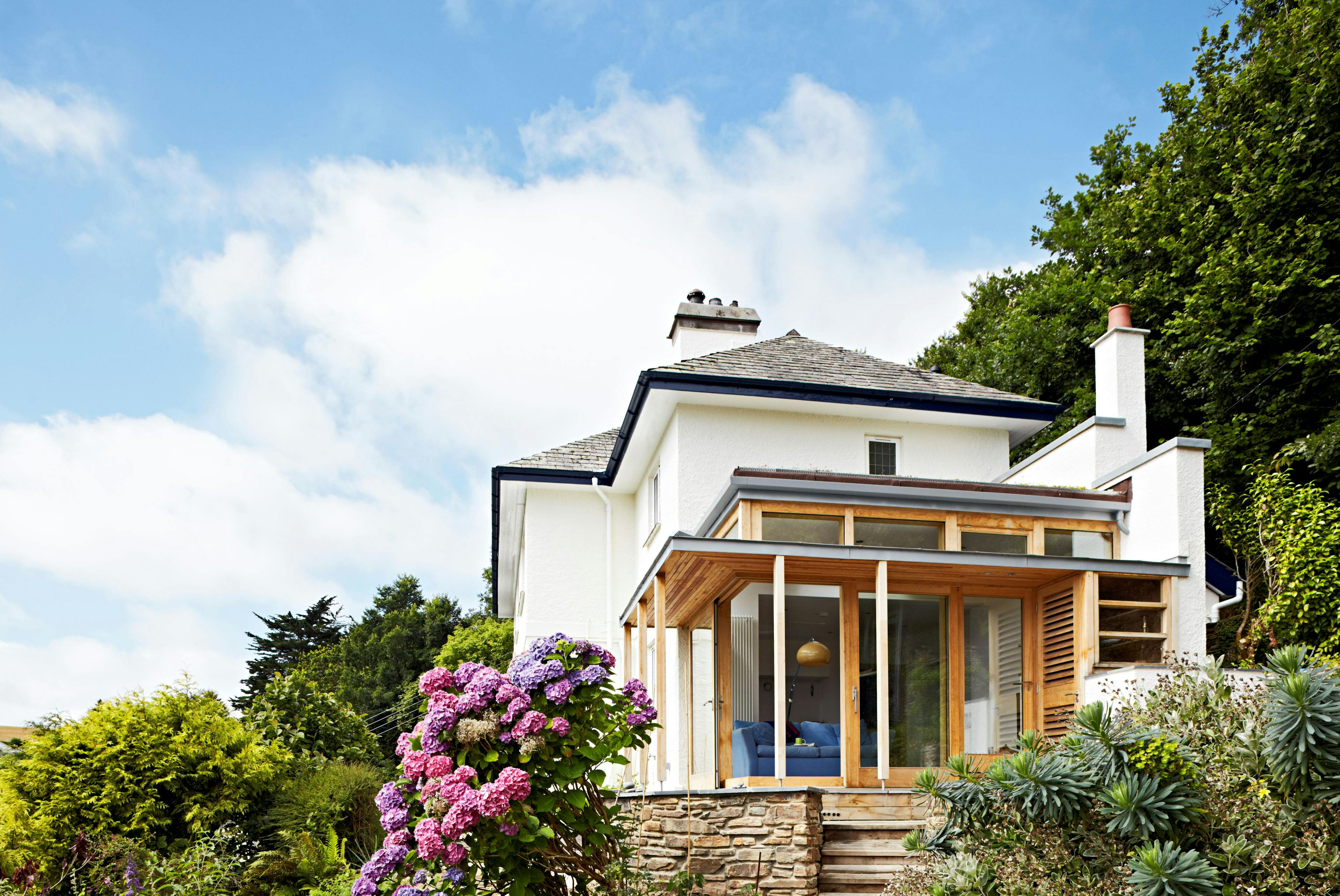A white house with a chestnut glulam extension set in a garden with blue skies behind