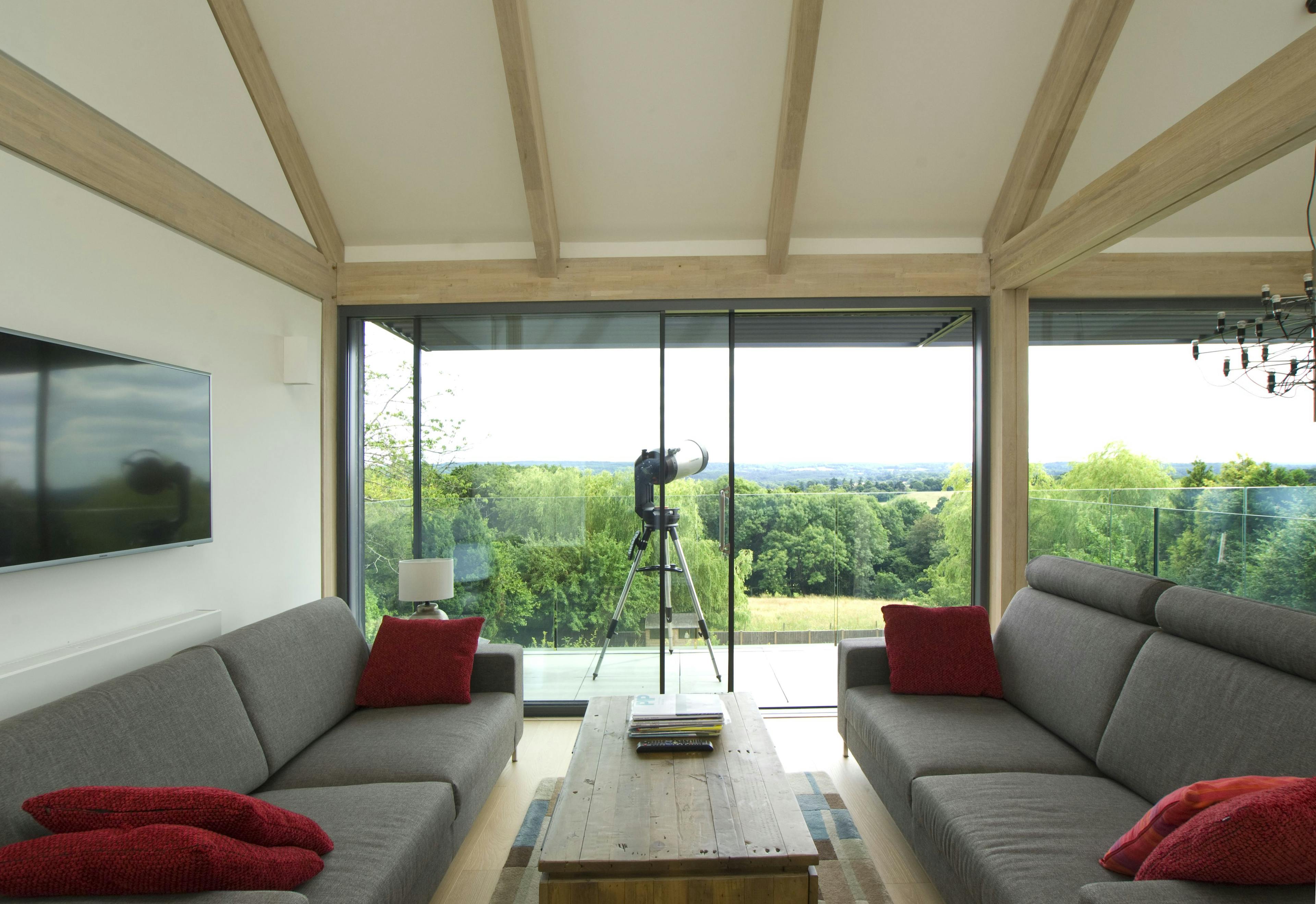 A mezzanine living room with sofas and views of the garden in an oak glulam framed house