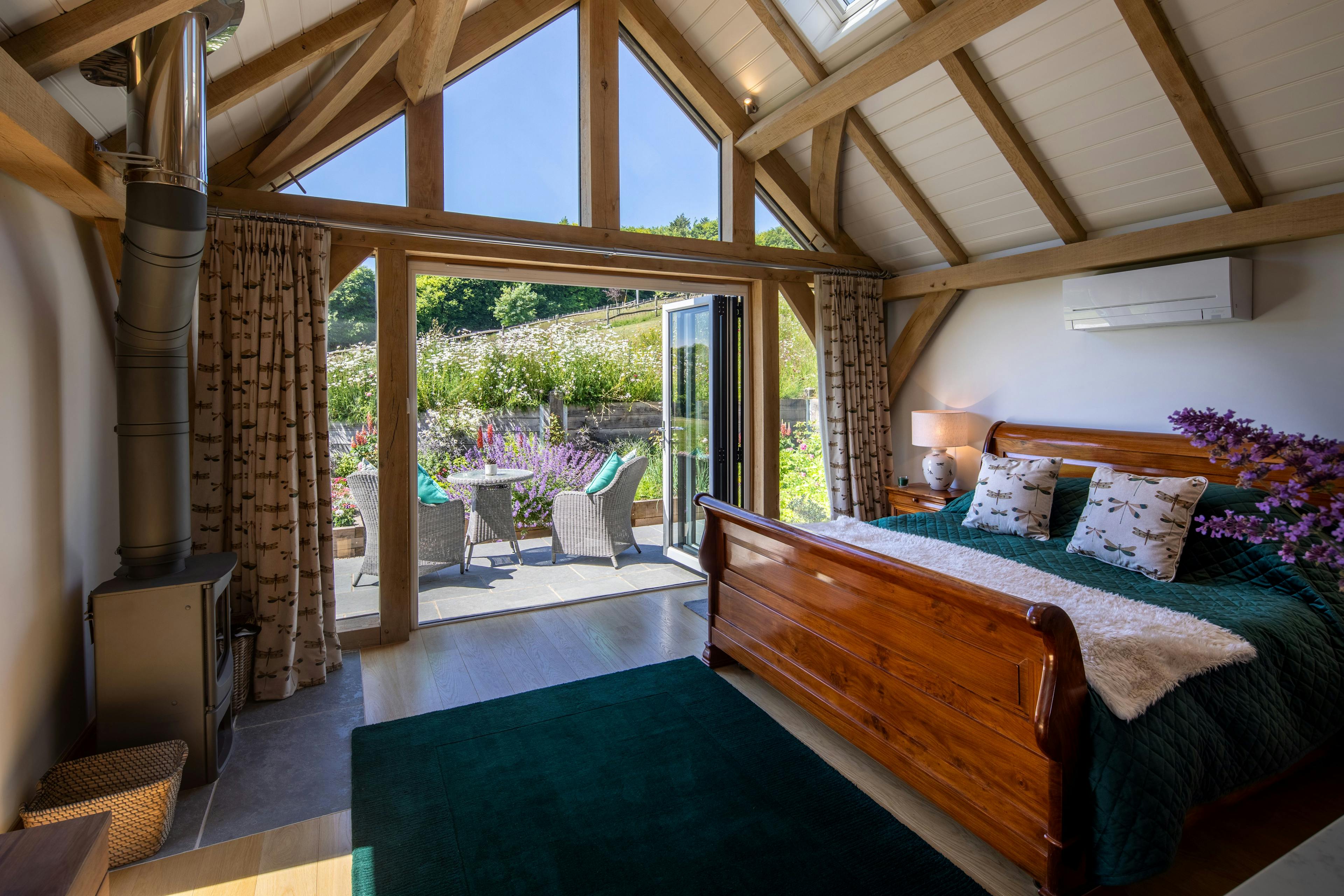 The bedroom area inside an oak framed garden annexe with a glazed gable end and doors opening to a patio