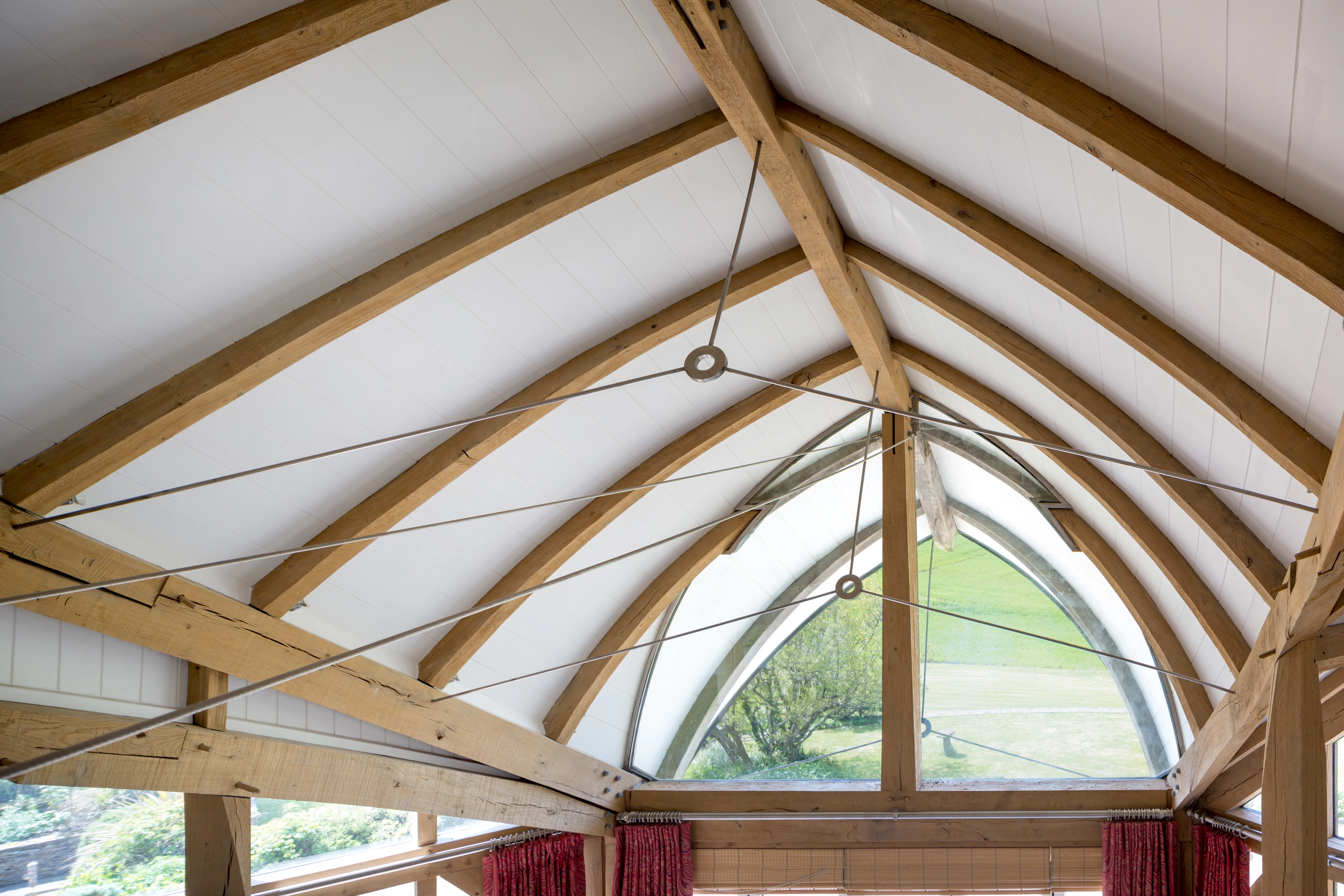Interior view of an open-plan family room with a boat-shaped oak-framed roof supported by steel tie rod fixings