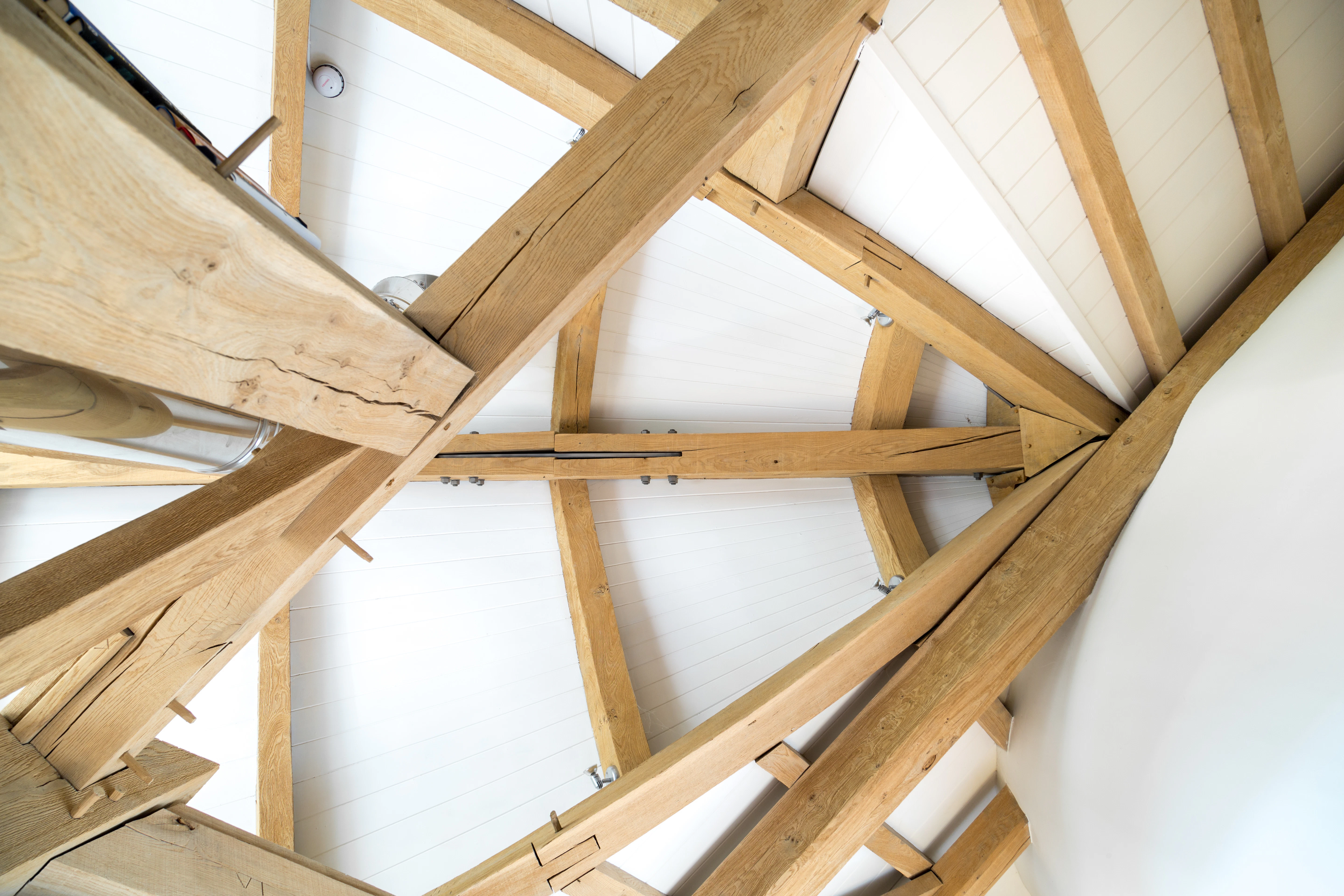 Internal close-up of an oak-framed boat roof, highlighting intricate traditional timber joinery paired with steel flitch plate connections
