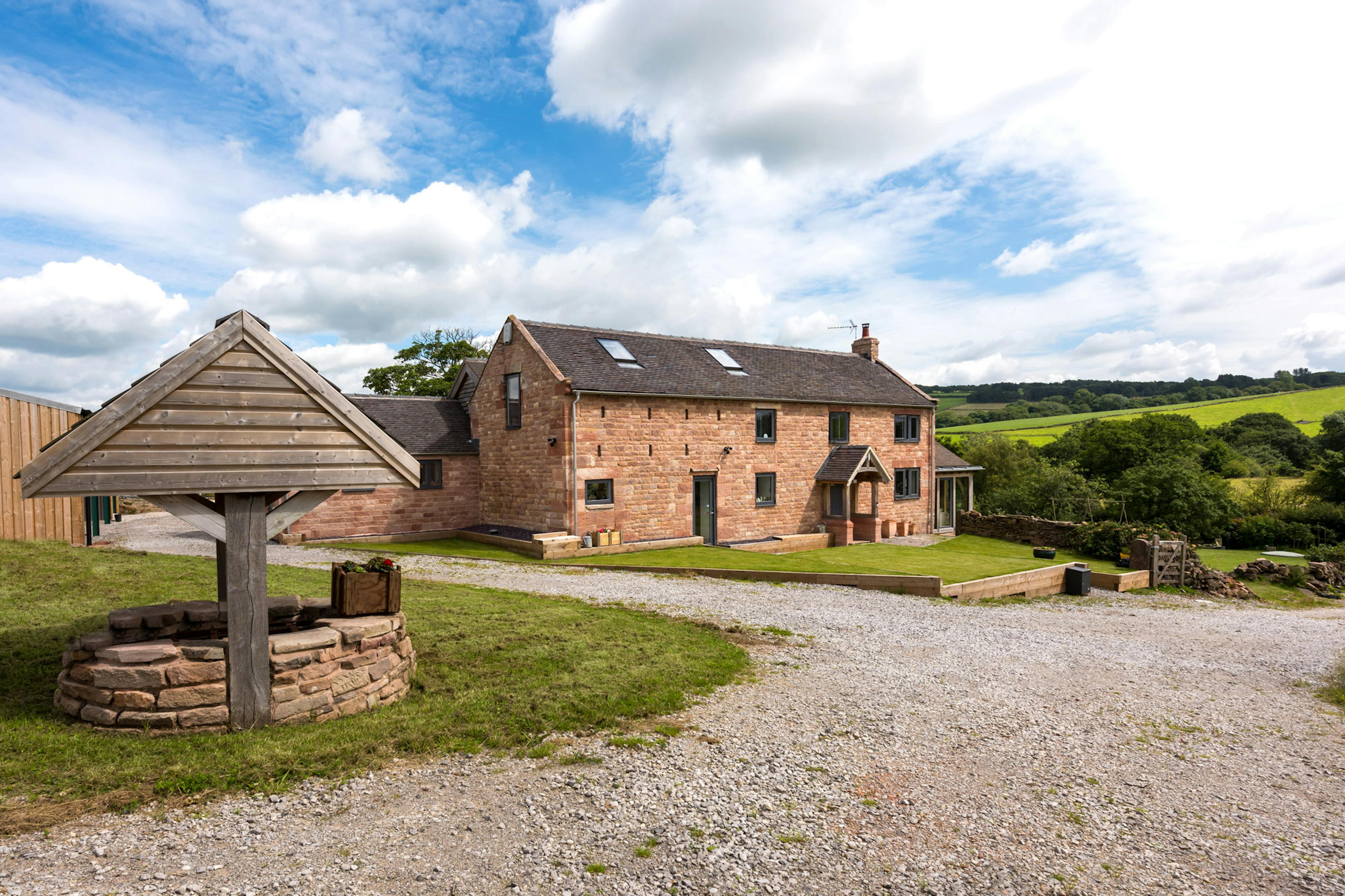 Exterior view of a farmhouse with oak-framed extensions set amidst countryside valleys