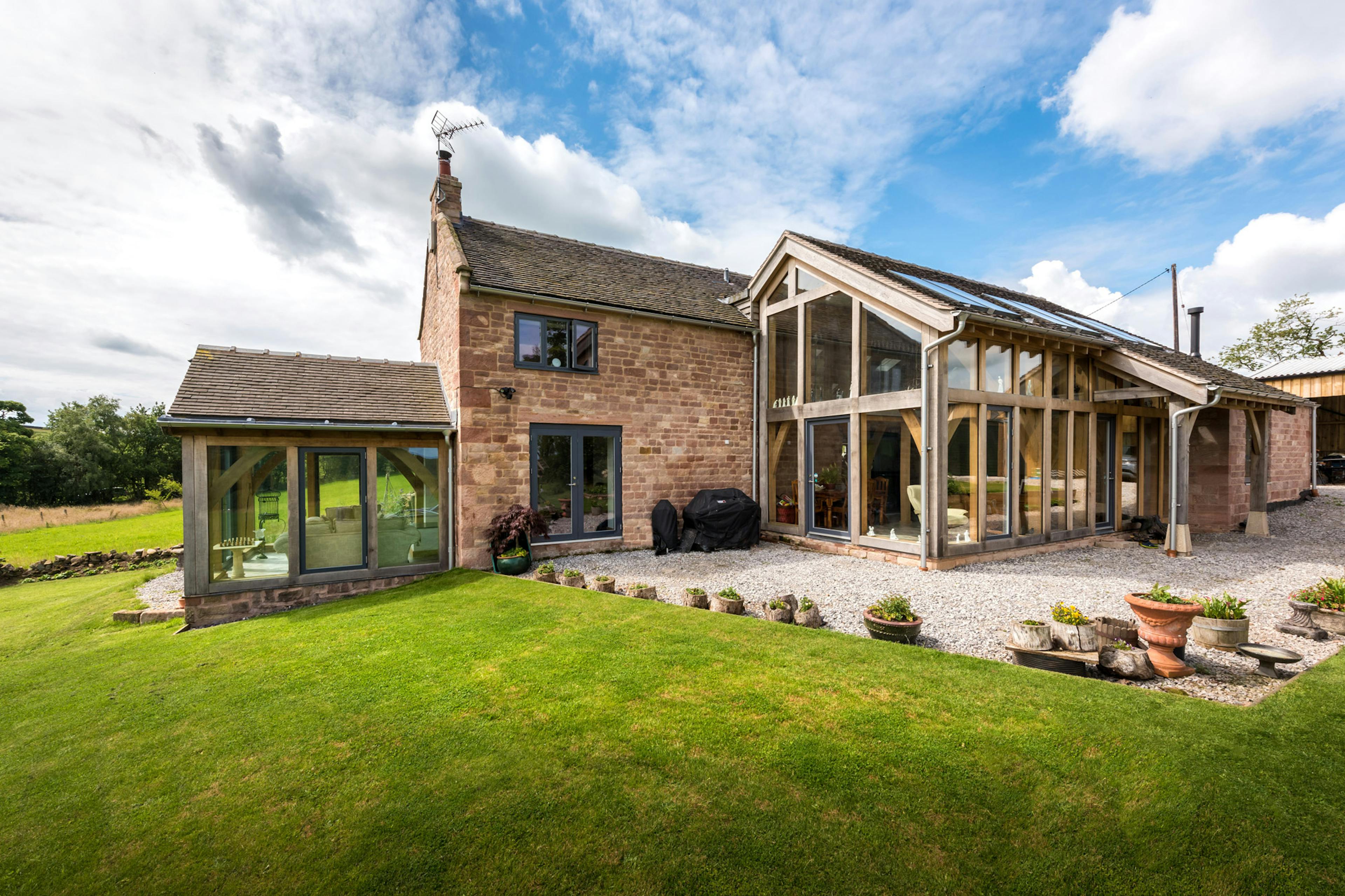 Exterior view of a two-story home with a rear extension consisting of a two-story glazed oak frame and an additional atrium