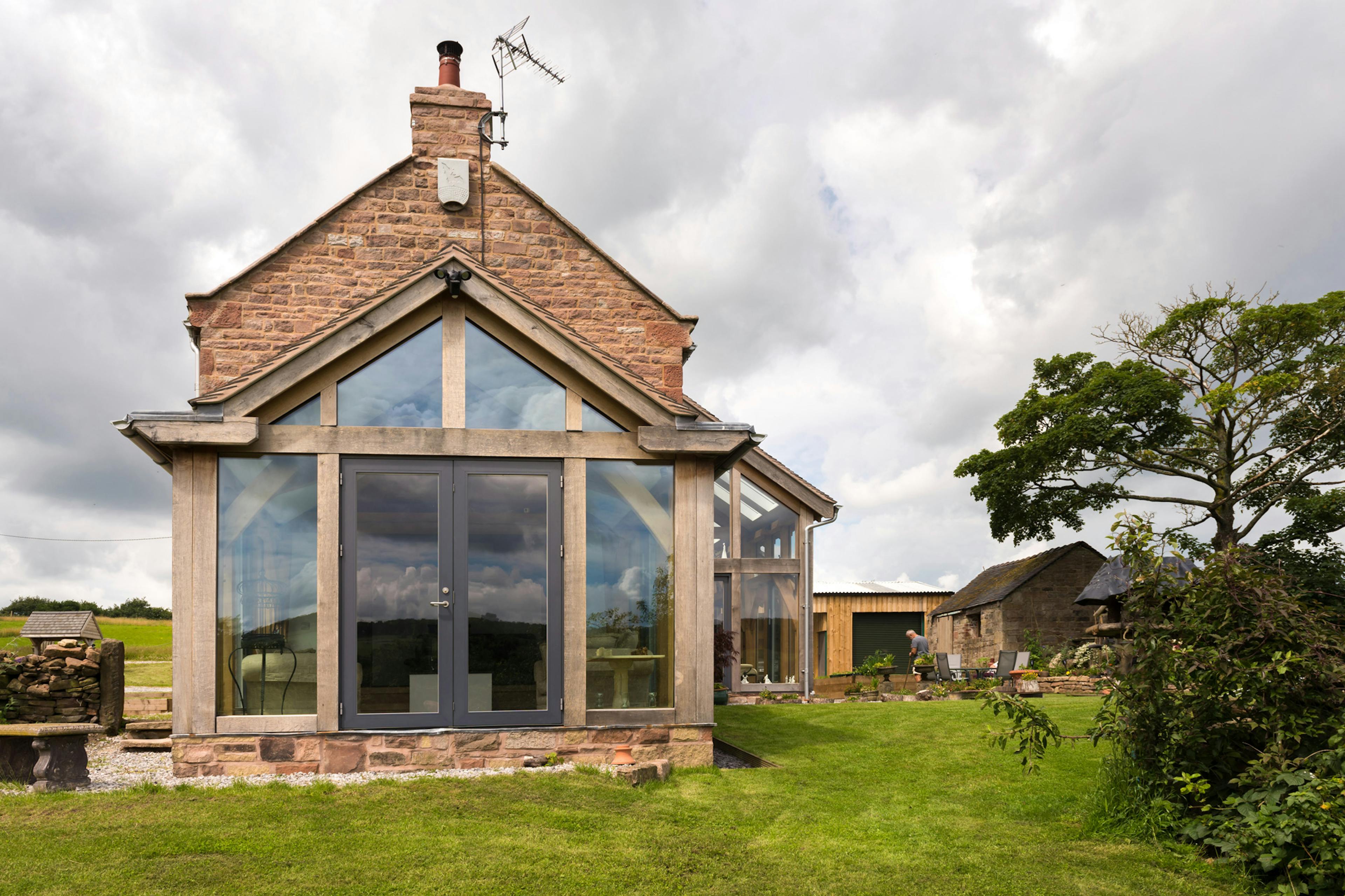 Exterior view of a newly renovated farmhouse showcasing an oak-framed, direct-glazed atrium