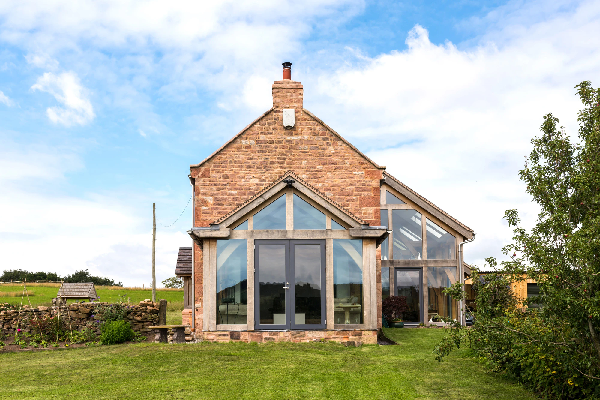Exterior view of a farmhouse-style, two-story home with an oak-framed lean-to extension and direct-glazed atrium.