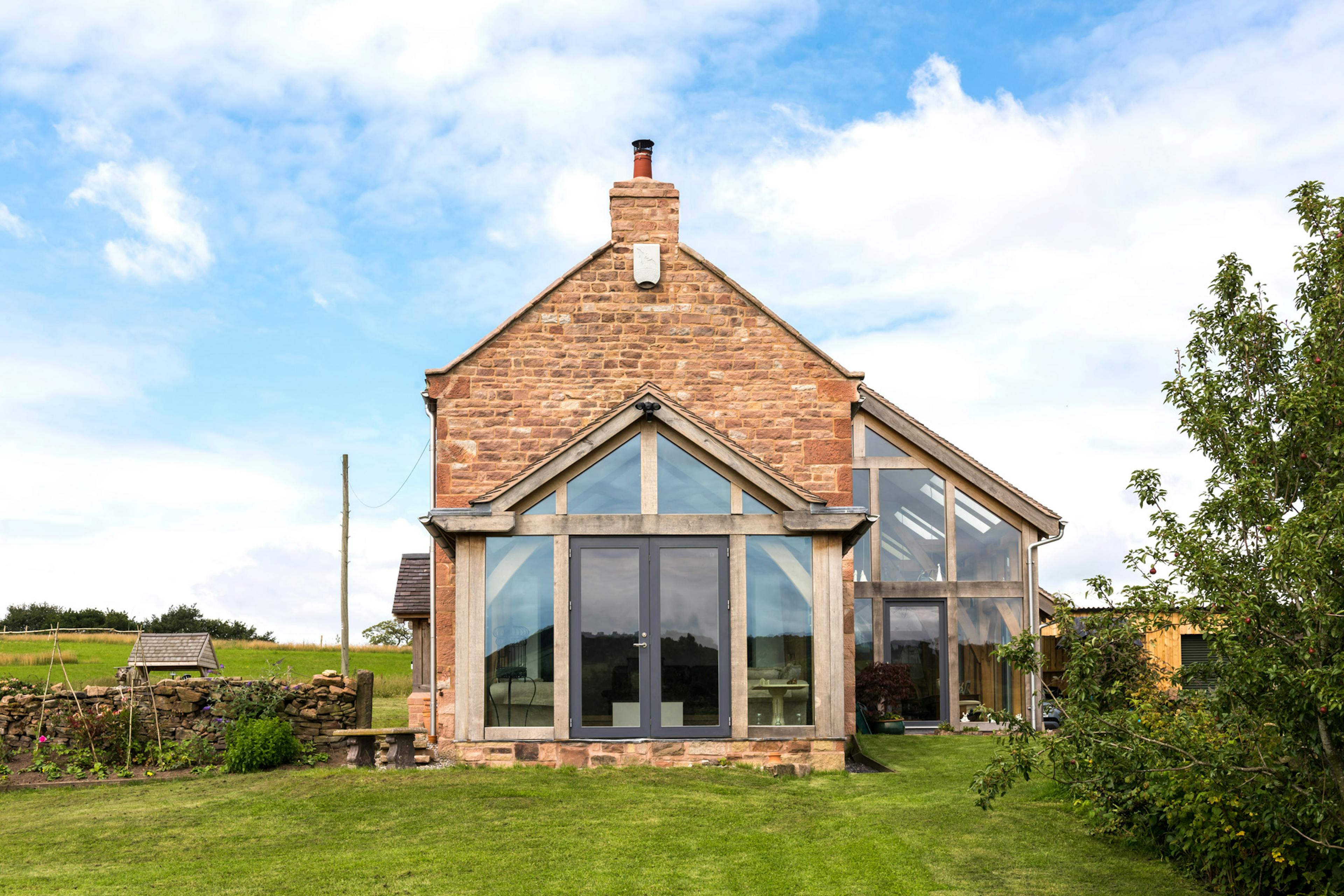 Exterior view of a farmhouse-style, two-story home with an oak-framed lean-to extension and direct-glazed atrium.
