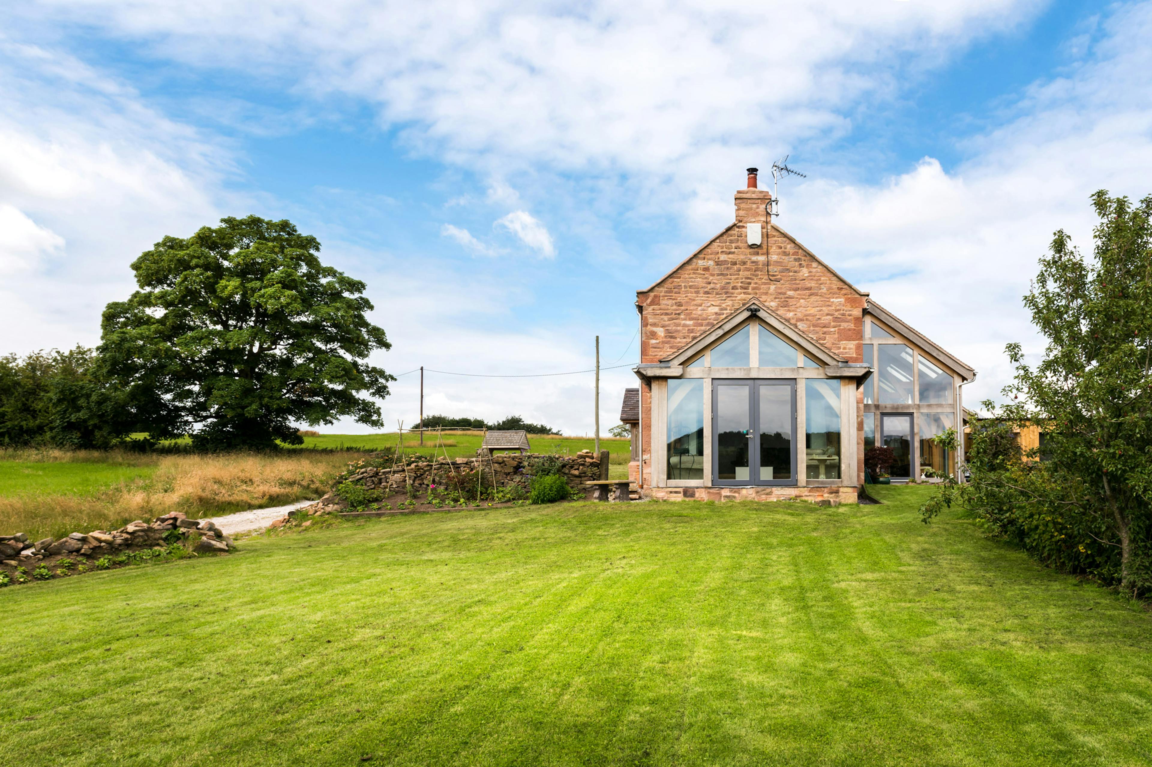 Exterior view of a two-story farmhouse featuring an oak-framed atrium in the countryside 