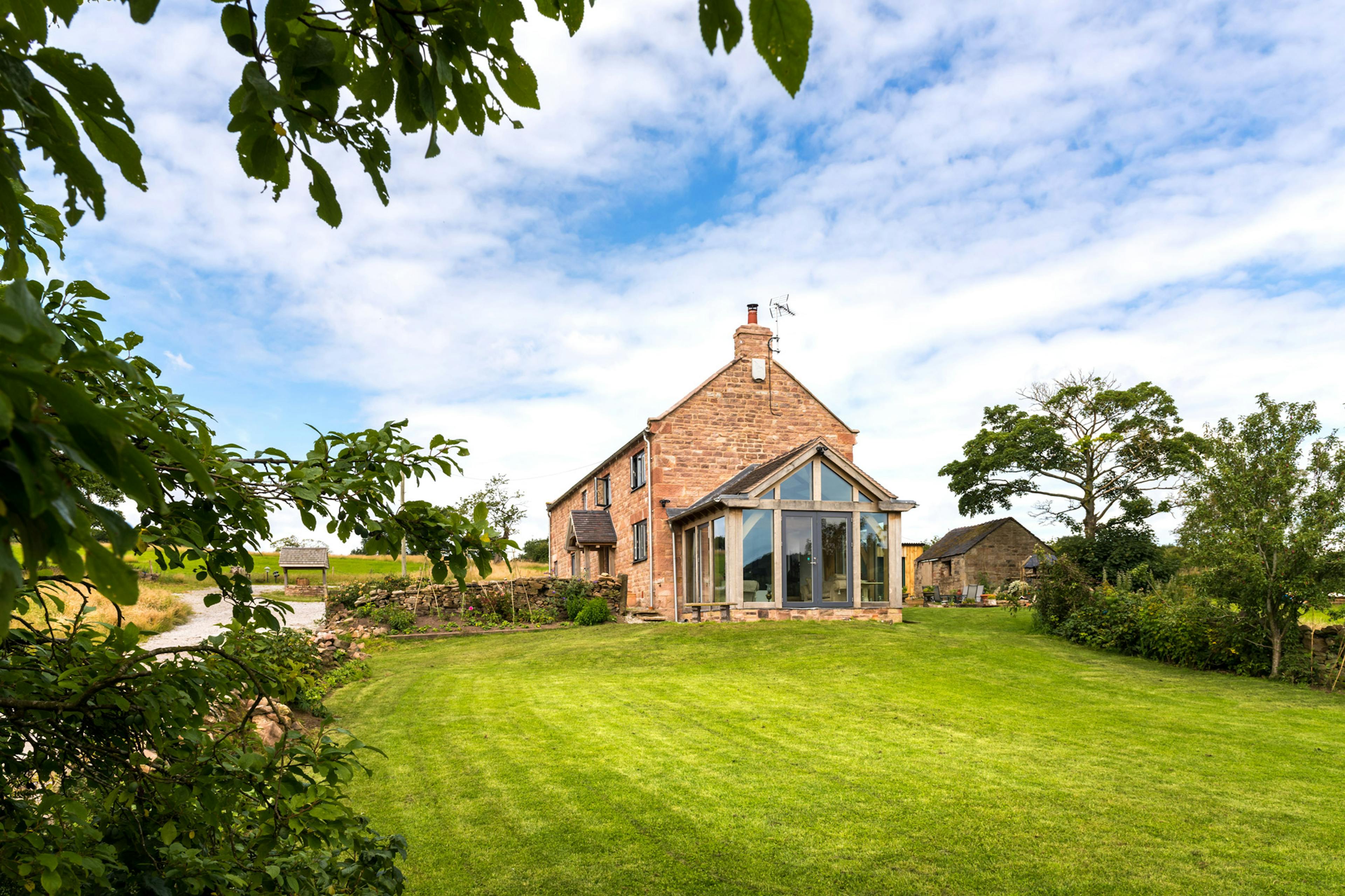 Exterior view of a two-story farmhouse featuring an oak-framed atrium and a countryside garden.