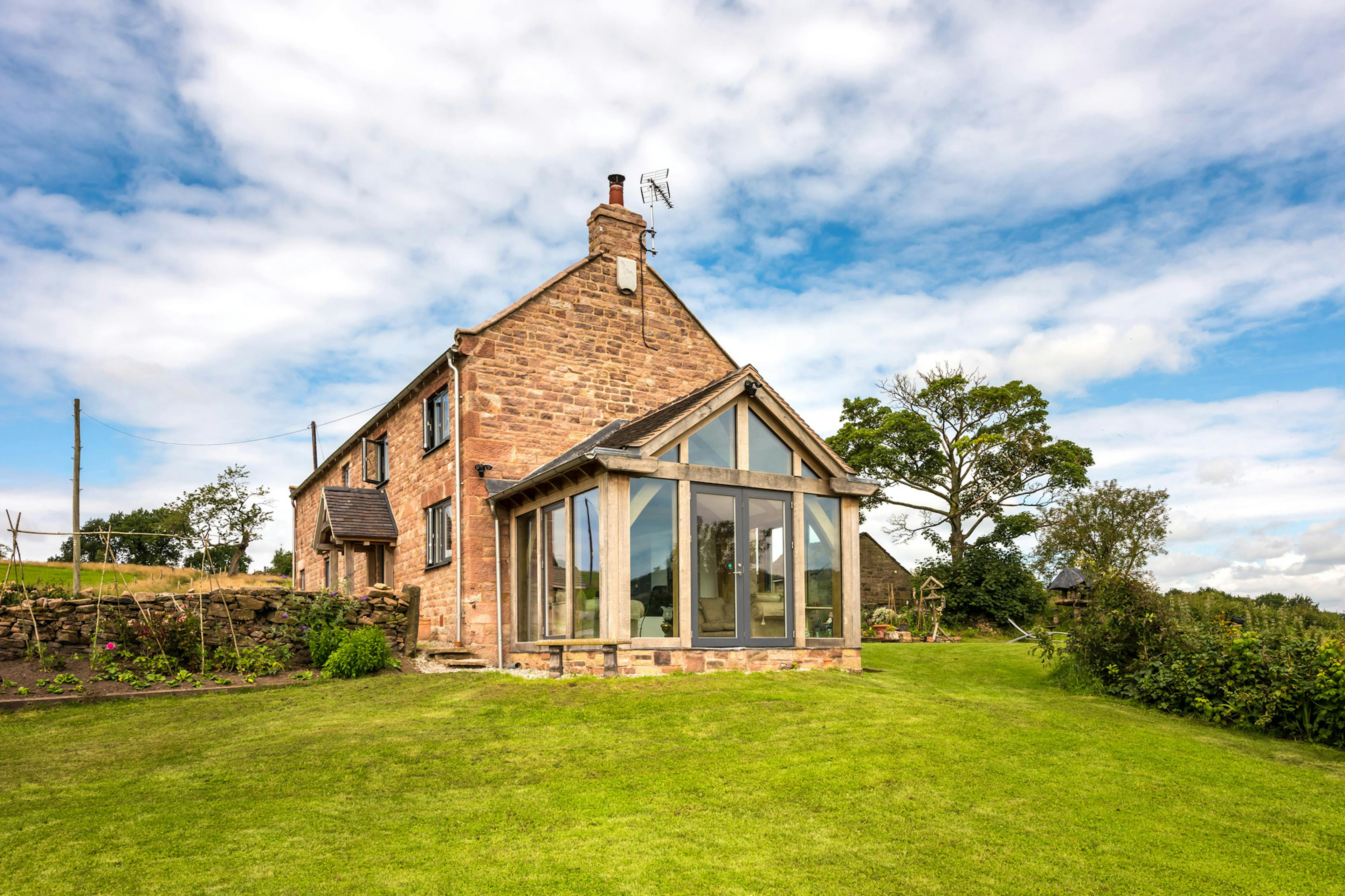 Exterior view of a two-story farmhouse with a direct-glazed oak-framed atrium.