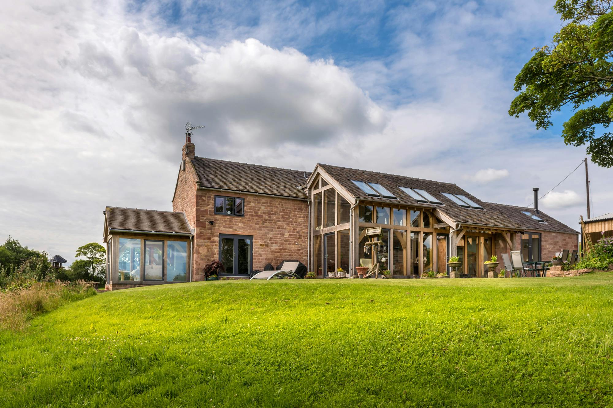 Exterior view of a two-story oak-framed lean-to extension and atrium with direct glazing.