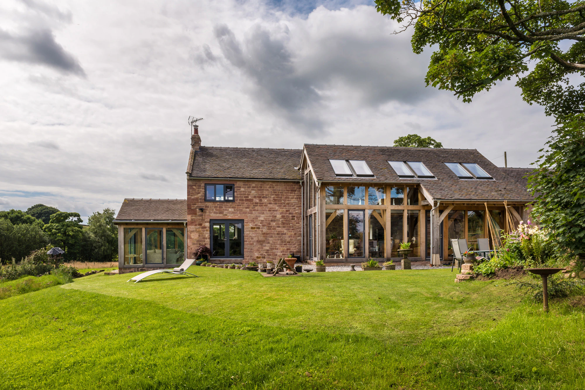 Exterior view of a two-story oak-framed lean-to extension with direct glazing