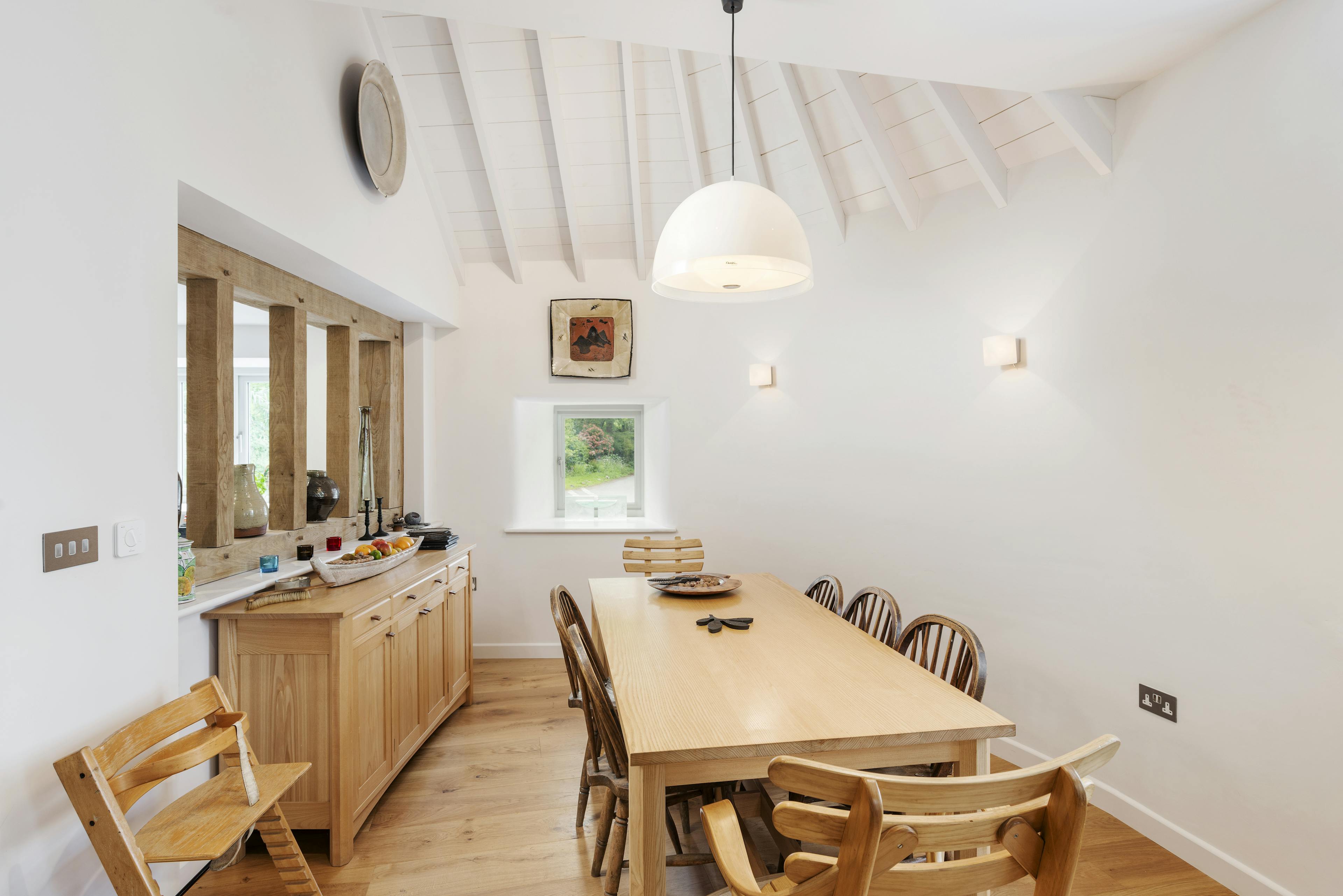 Interior view of an elegant dining room featuring oak-framed wall divider windows leading to the kitchen and a white-painted clad ceiling