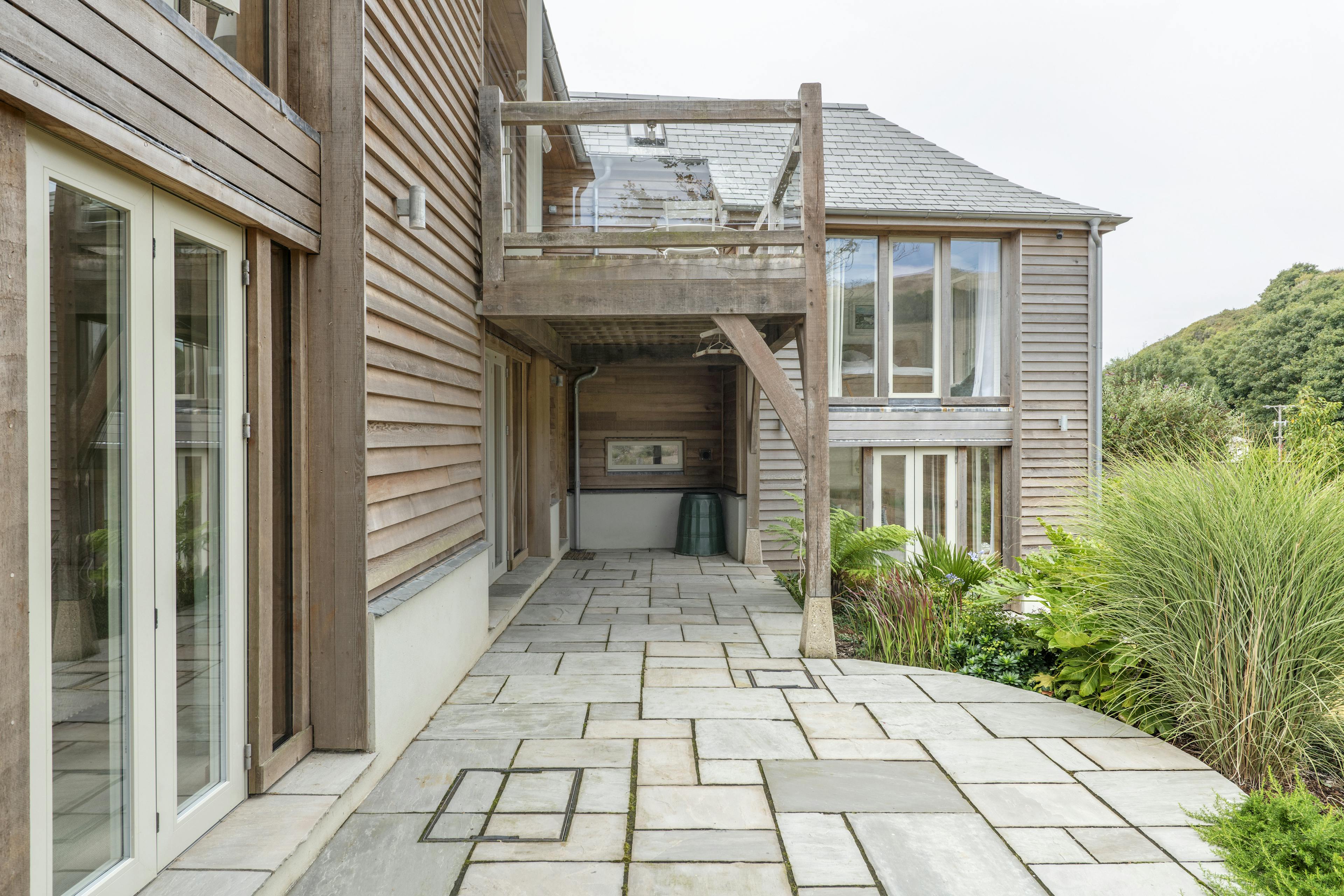 A timber clad home with a an oak framed balcony over a paved area