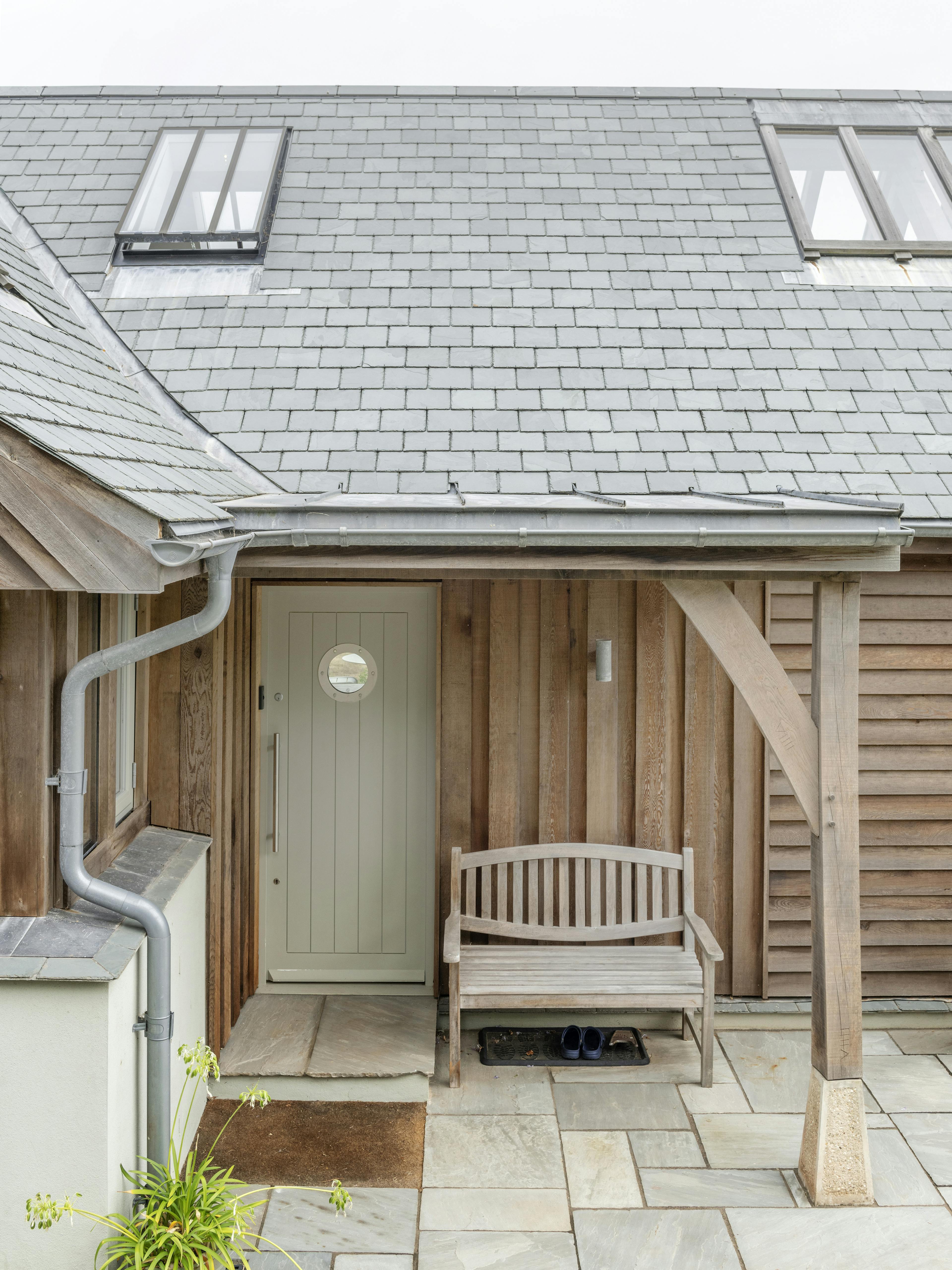 A timber clad home showing a front door with an oak porch and patio