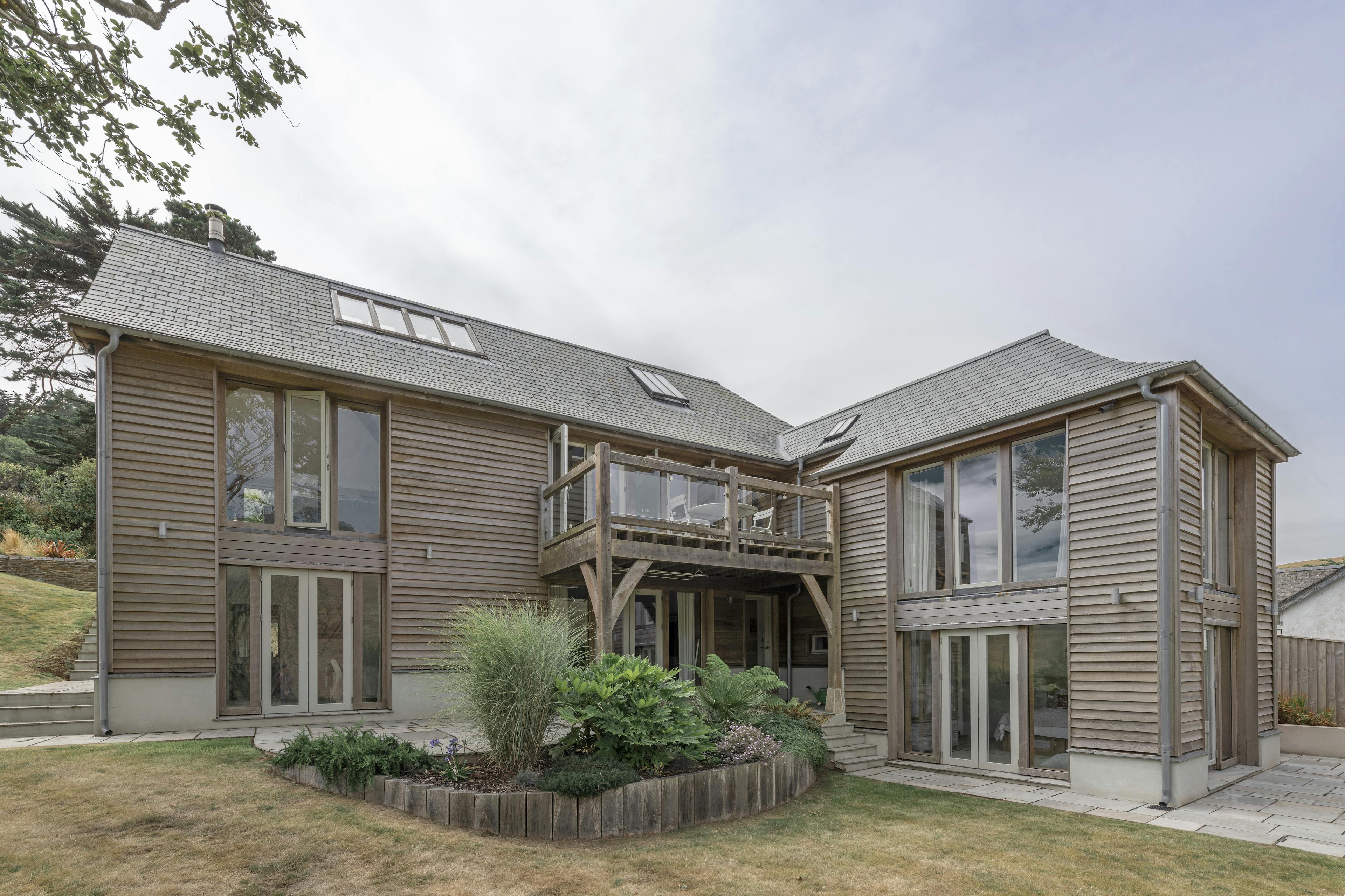 A timber clad home with an oak balcony, surrounded by landscaped gardens