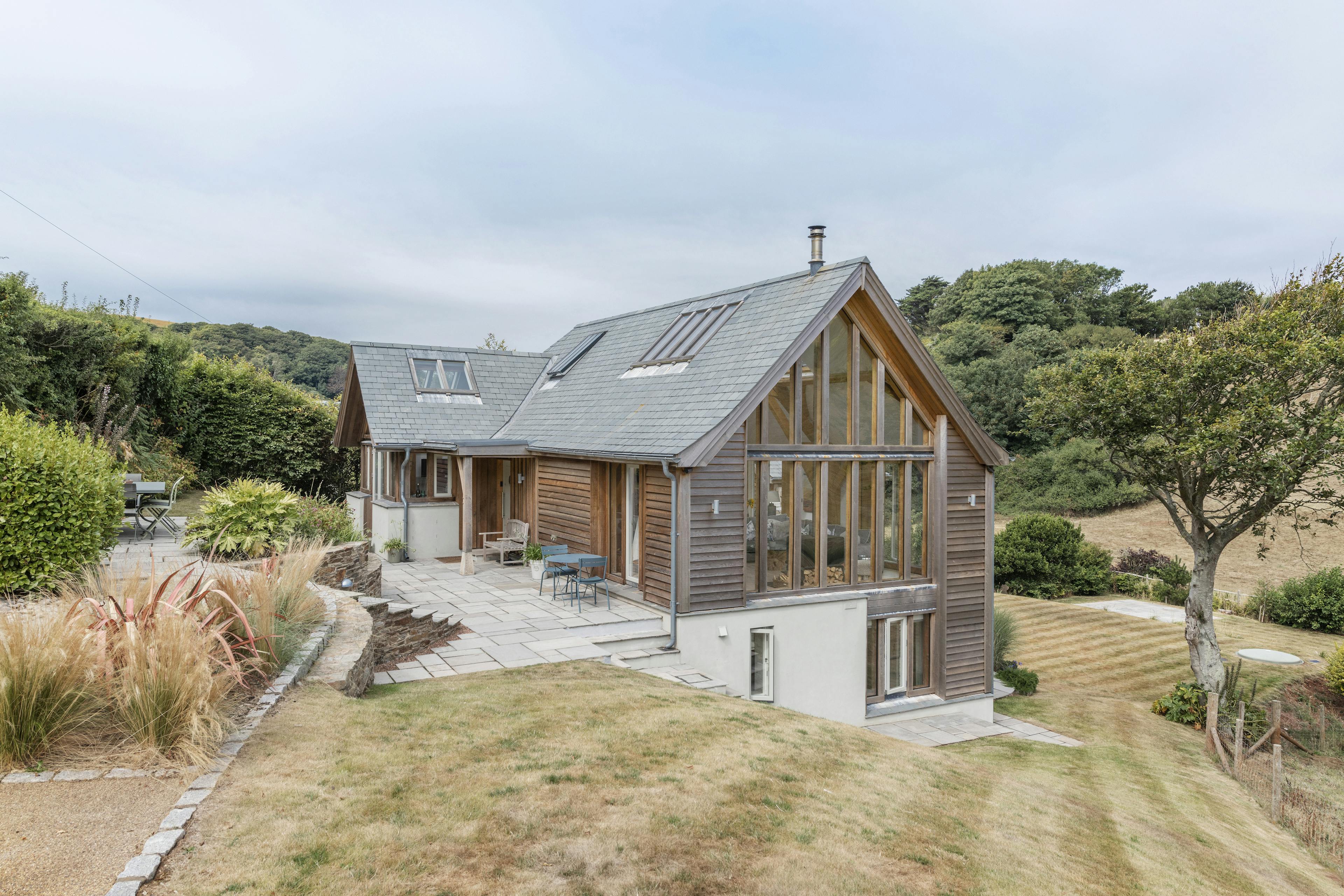 A timber clad home with a glazed gable end, surrounded by landscaped gardens