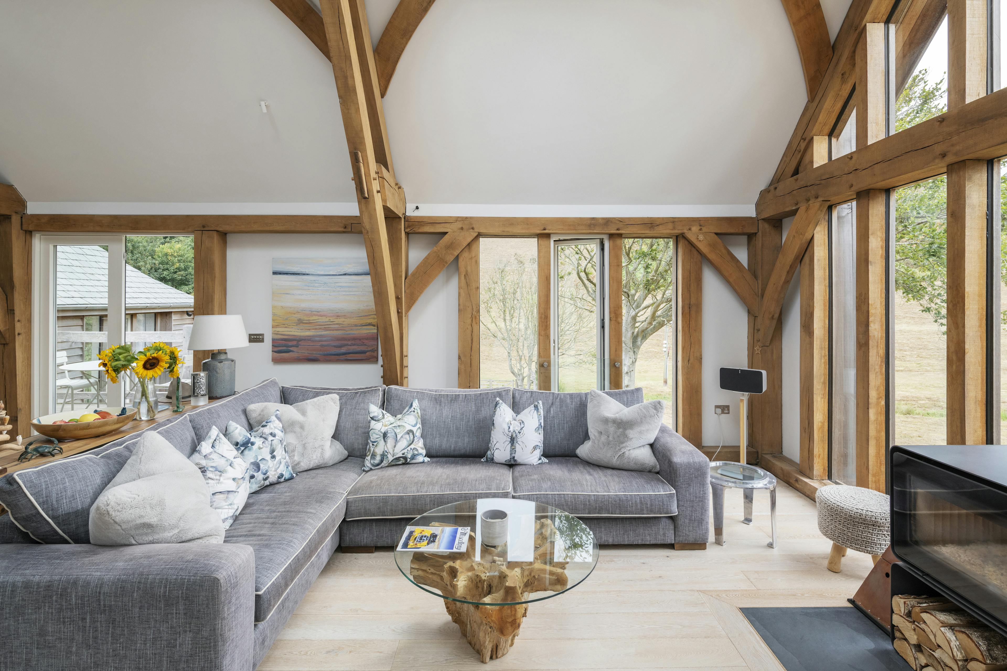 A modern oak framed sitting area showing a sofa and log burner, with a glazed gable end