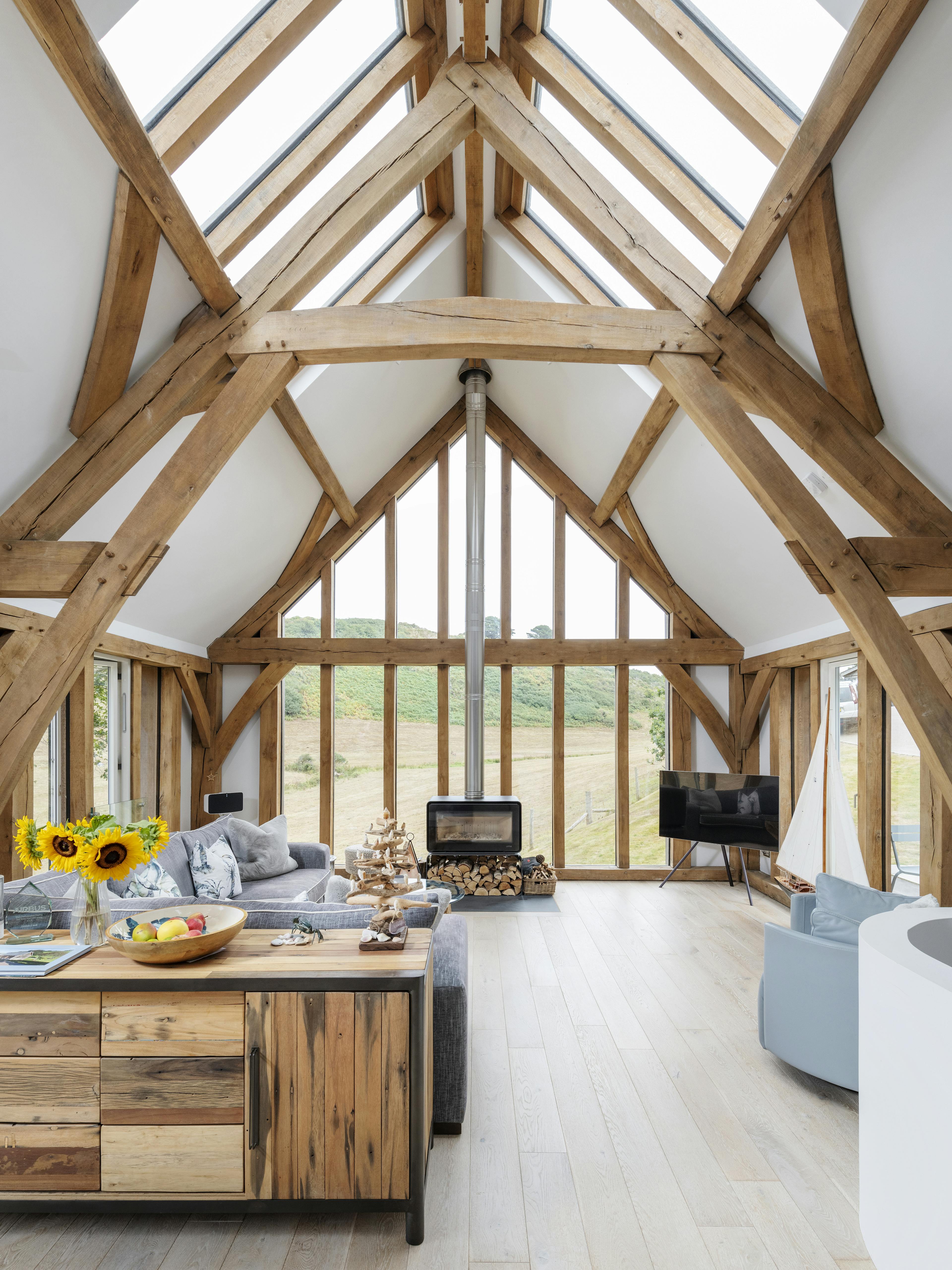 A modern, light filled oak framed home with a glazed gable end and rooflights, showing an open plan living area and log burner