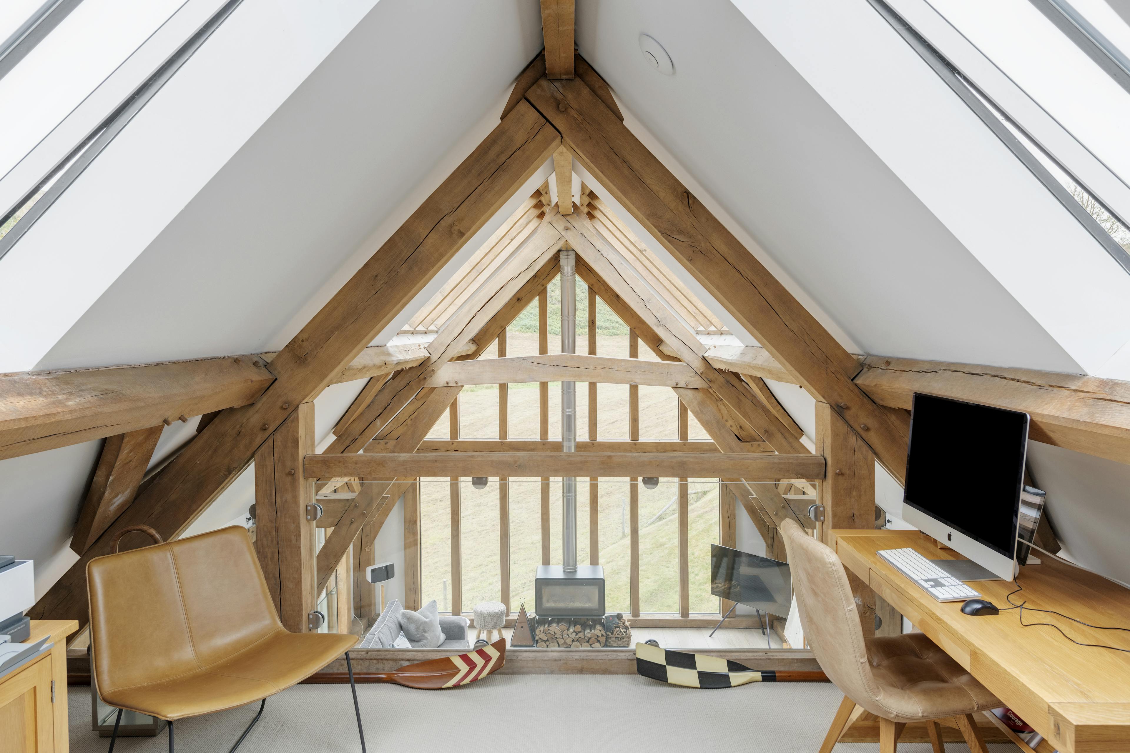 A mezzanine in an oak framed house with an open plan living area below and glazed gable end