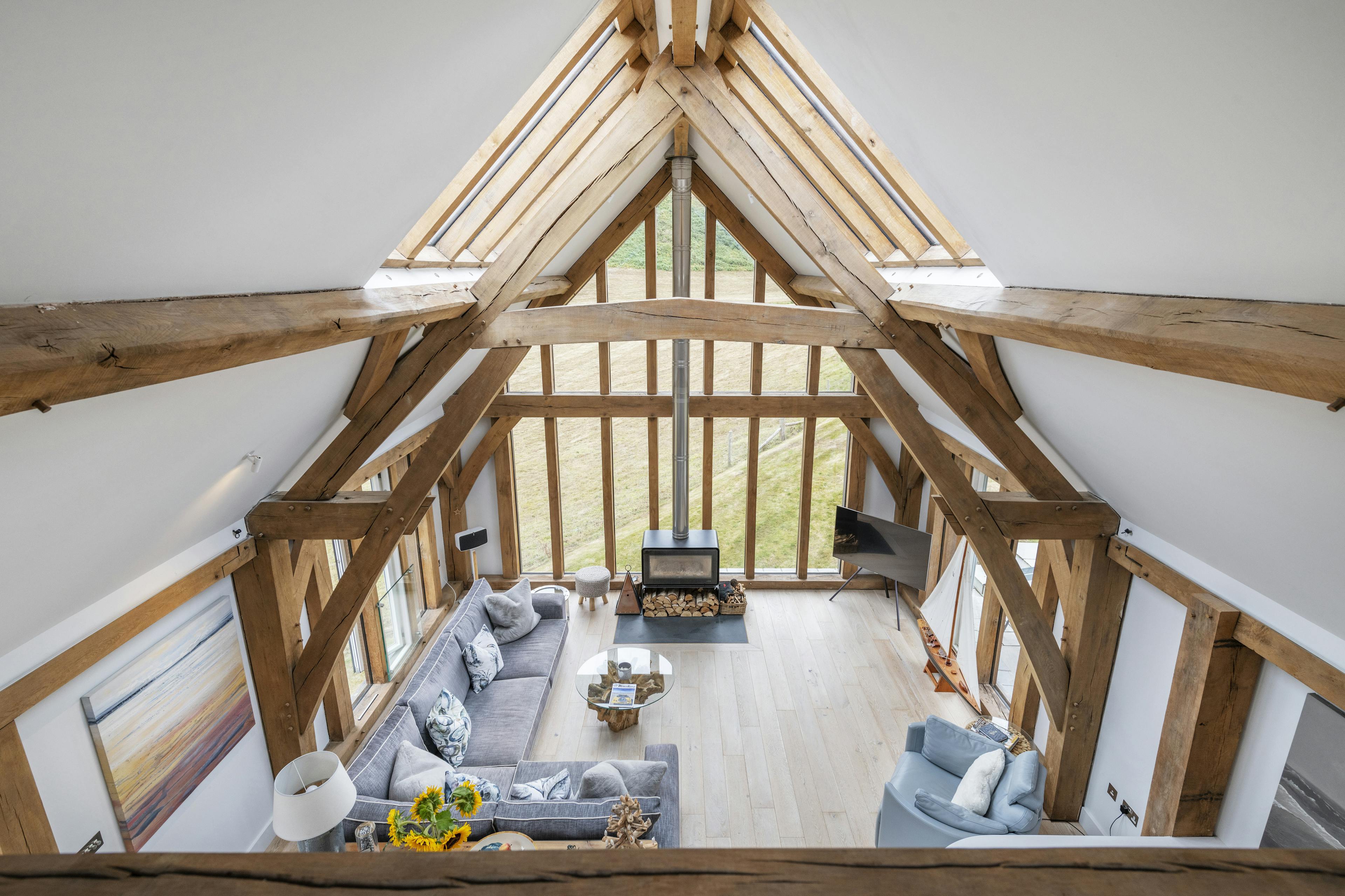 A mezzanine in an oak framed house with an open plan living area below and glazed gable end