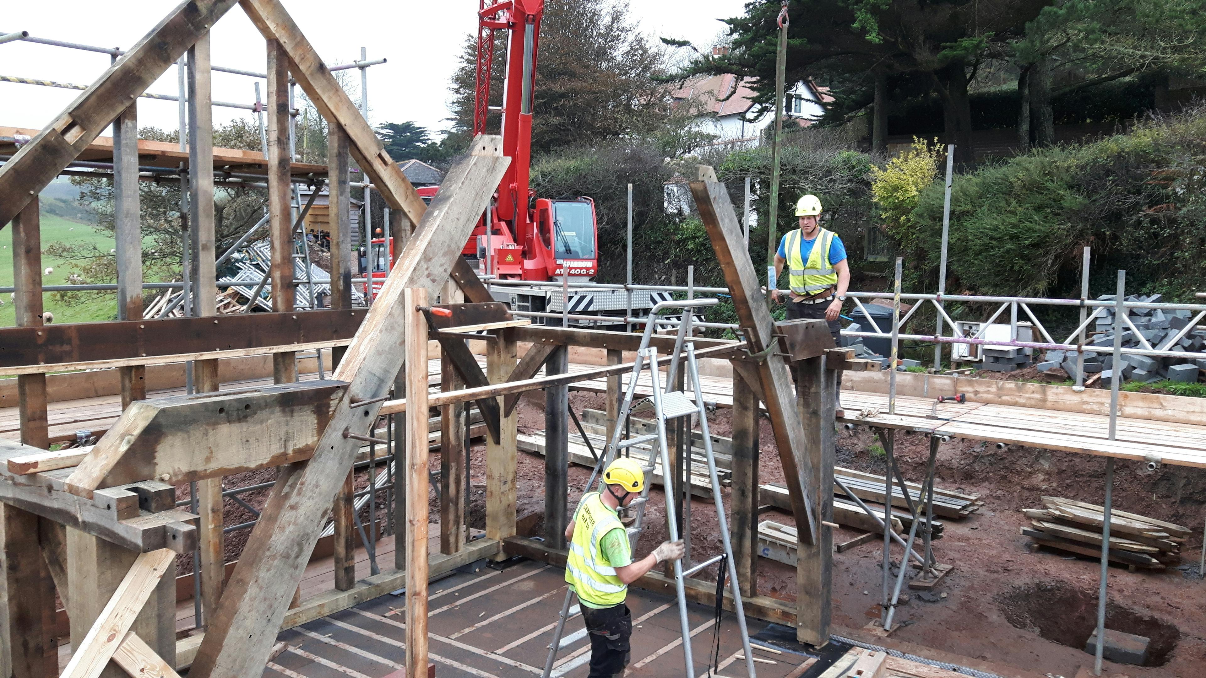 An oak frame being installed on a building site by carpenters