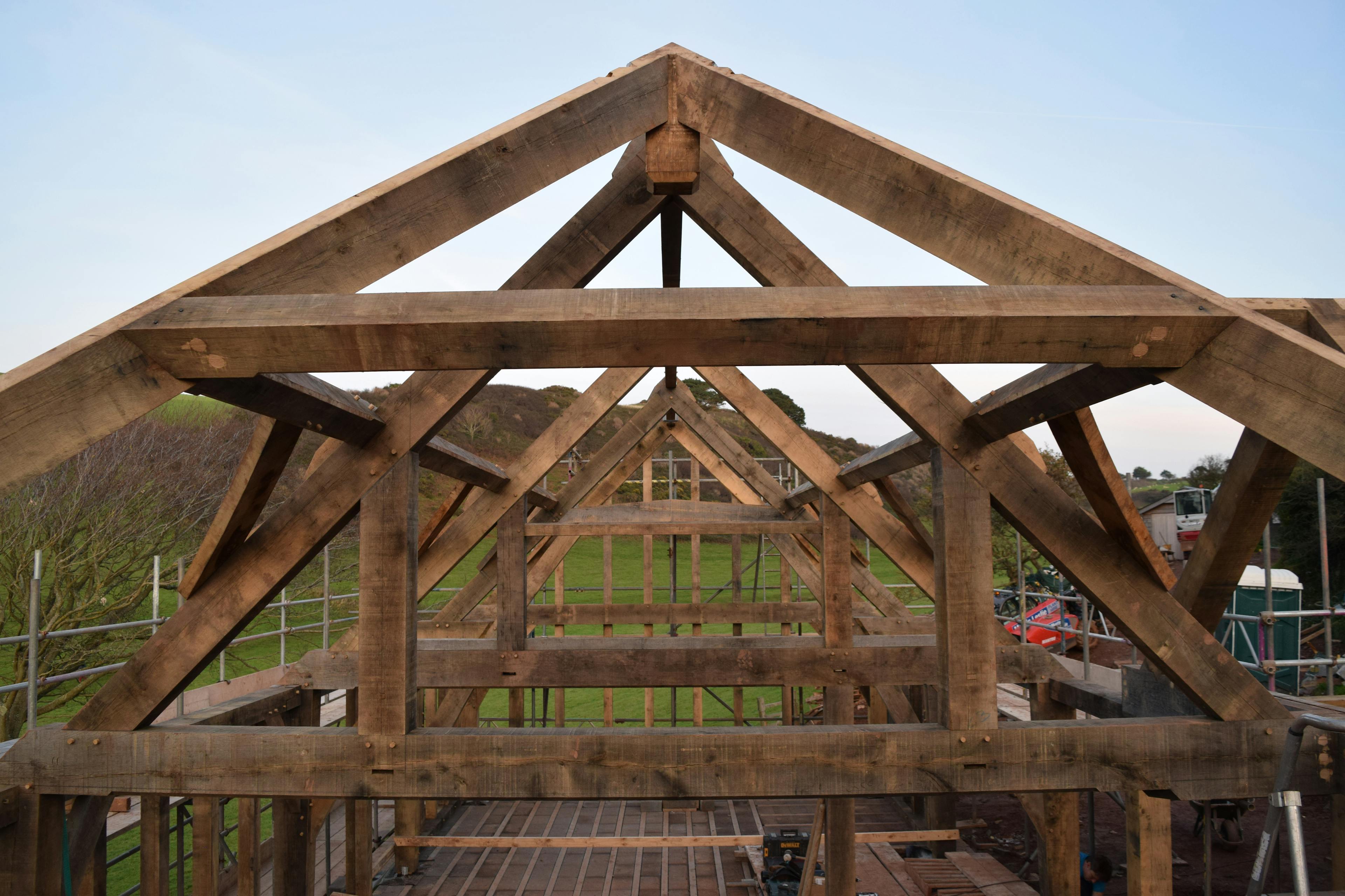 An oak frame being installed on a building site with green fields behind and a blue sky