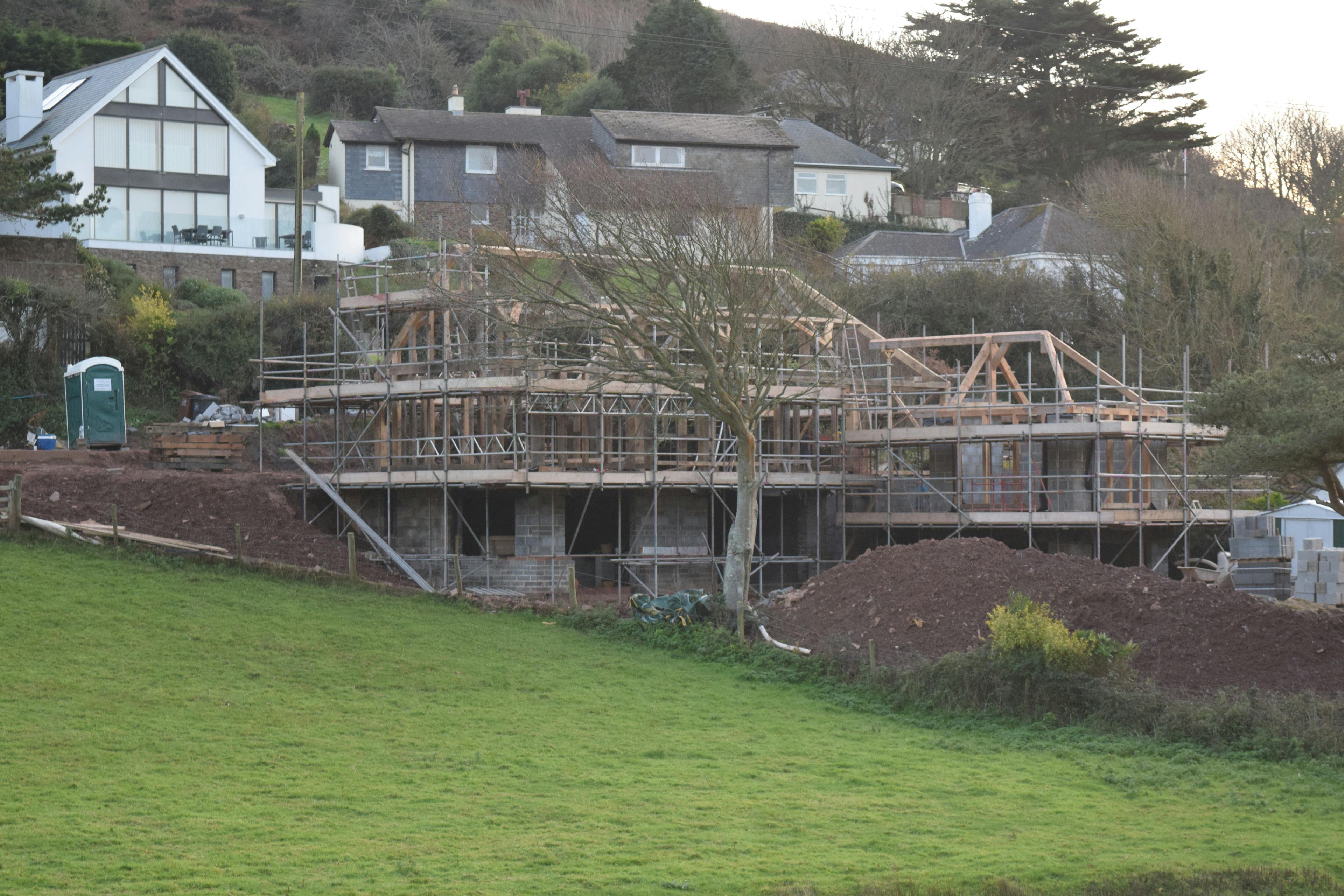 An oak frame being installed on a building site with green fields in front