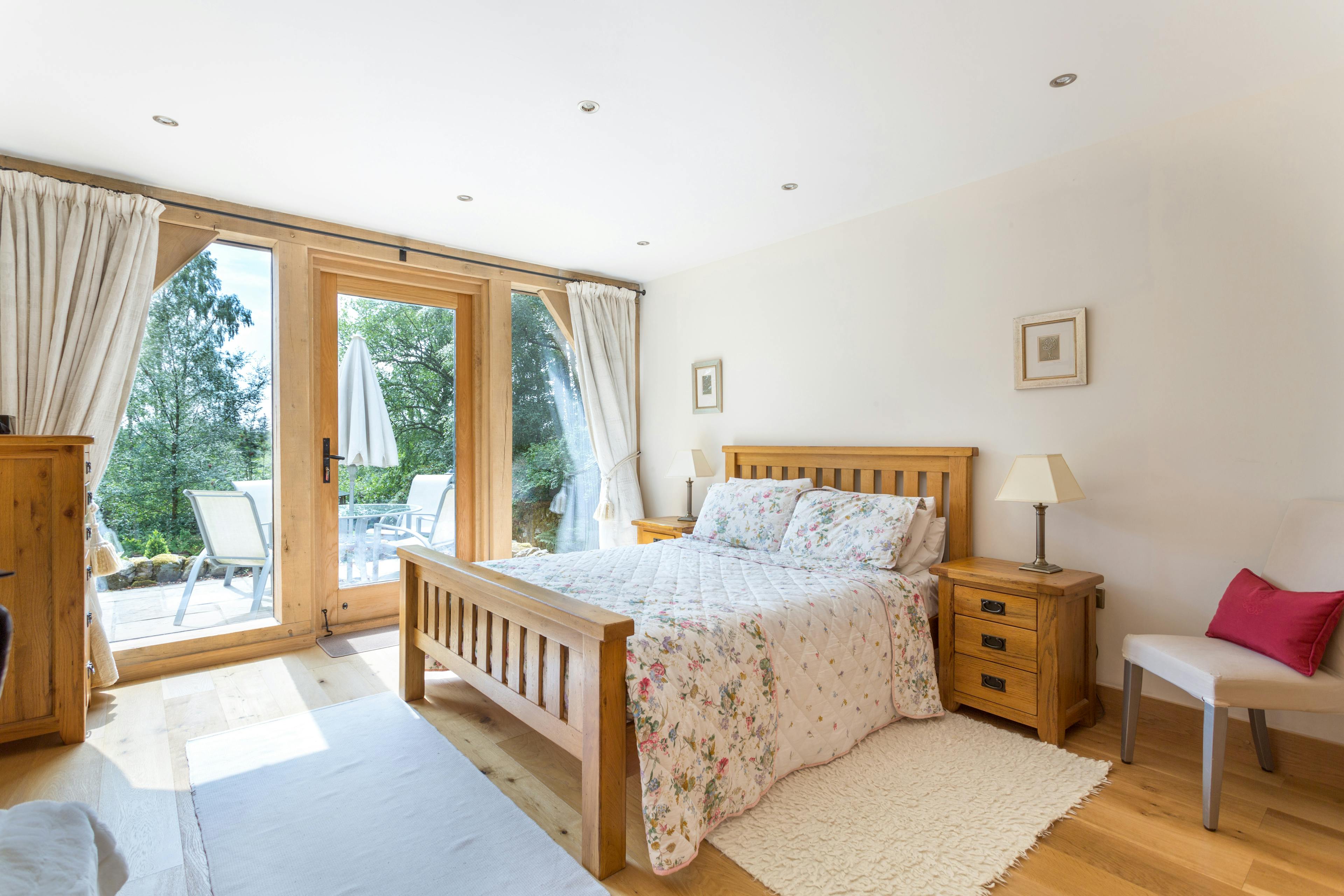 An oak framed bedroom with a large floor to ceiling window and door looking out onto a patio